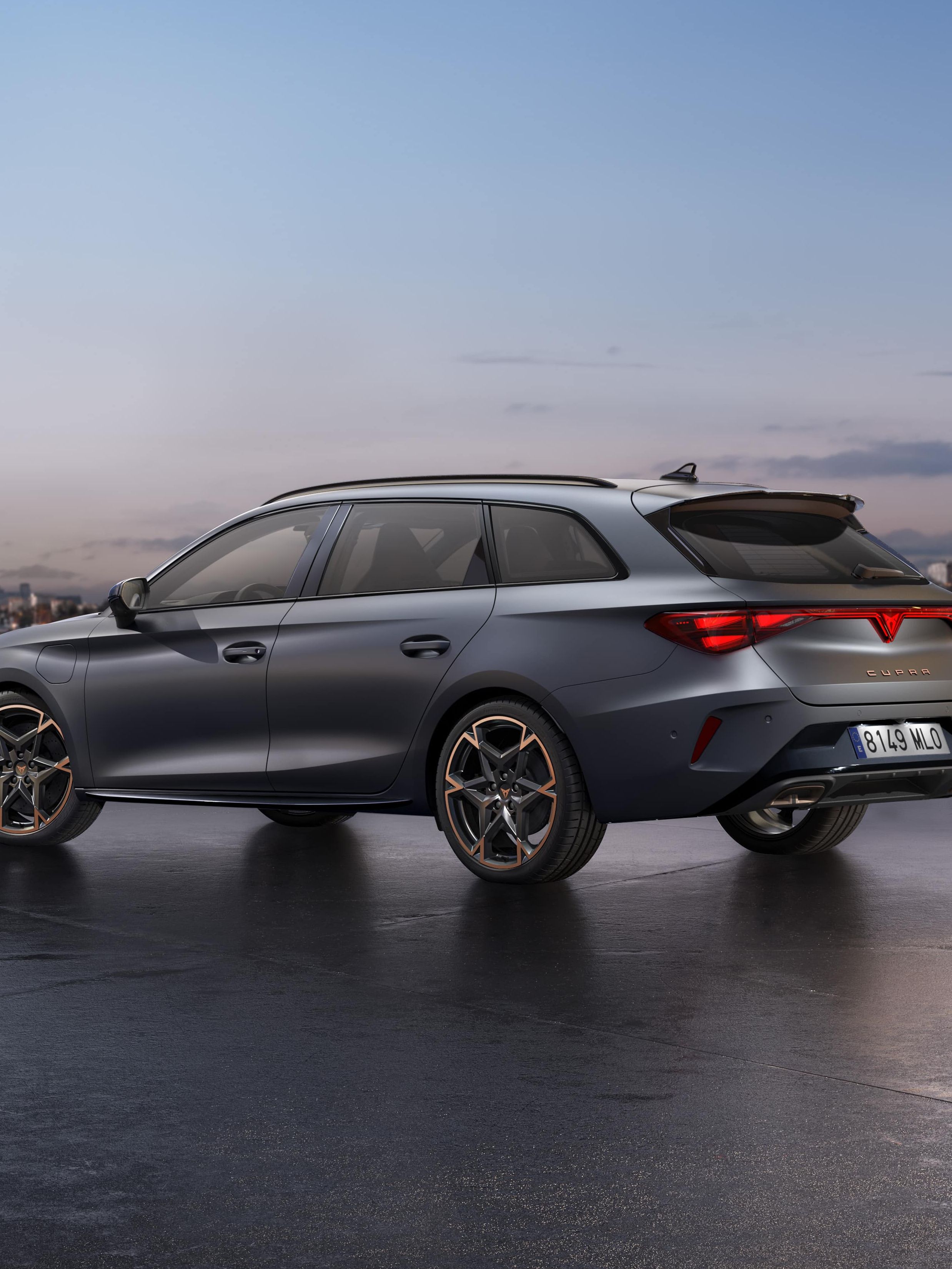 CUPRA LEON SPORTSTOURER stoji ob obali ob sončnem zahodu. V ozadju je mestno obzorje z visokimi stavbami, mokra površina pod vozilom pa odseva nebo.