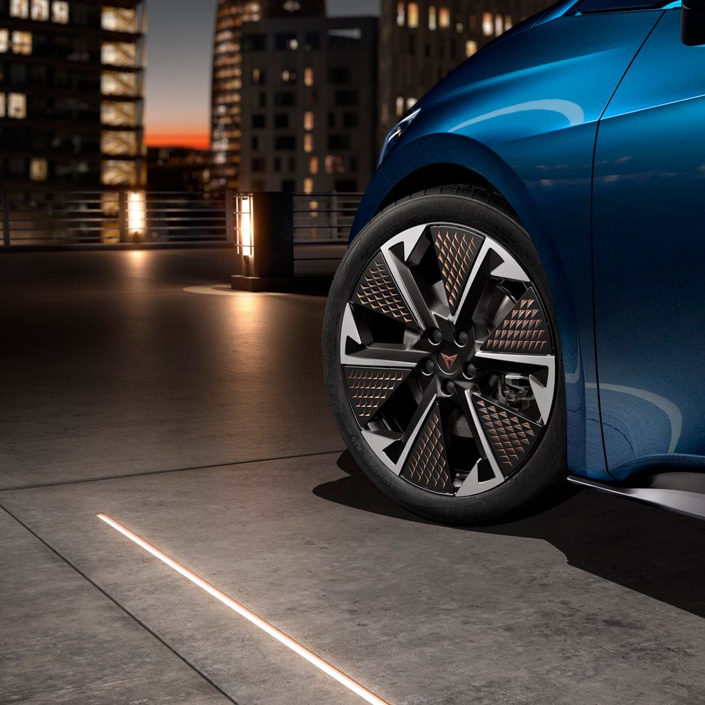 Kolo avtomobila CUPRA Born z modernim dizajnom, parkirano ob mestnem naključju ob večernem času. V ozadju se vidijo osvetljene stavbe.