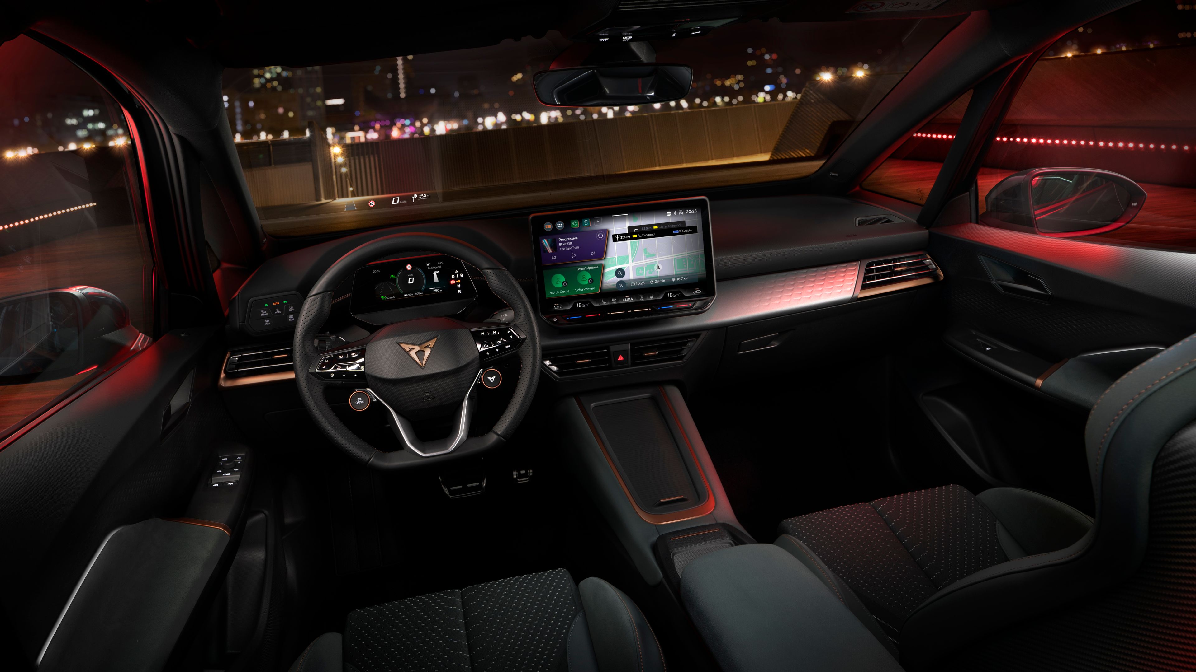 Notranjost sodobnega avtomobila CUPRA Born prikazuje osvetljeno armaturo z osrednjim digitalnim zaslonom na dotik in športnim volanom. V ozadju se skozi okna vidi mesto ponoči. Osvetlitev je rdeče barve, kar daje notranjosti futurističen videz.