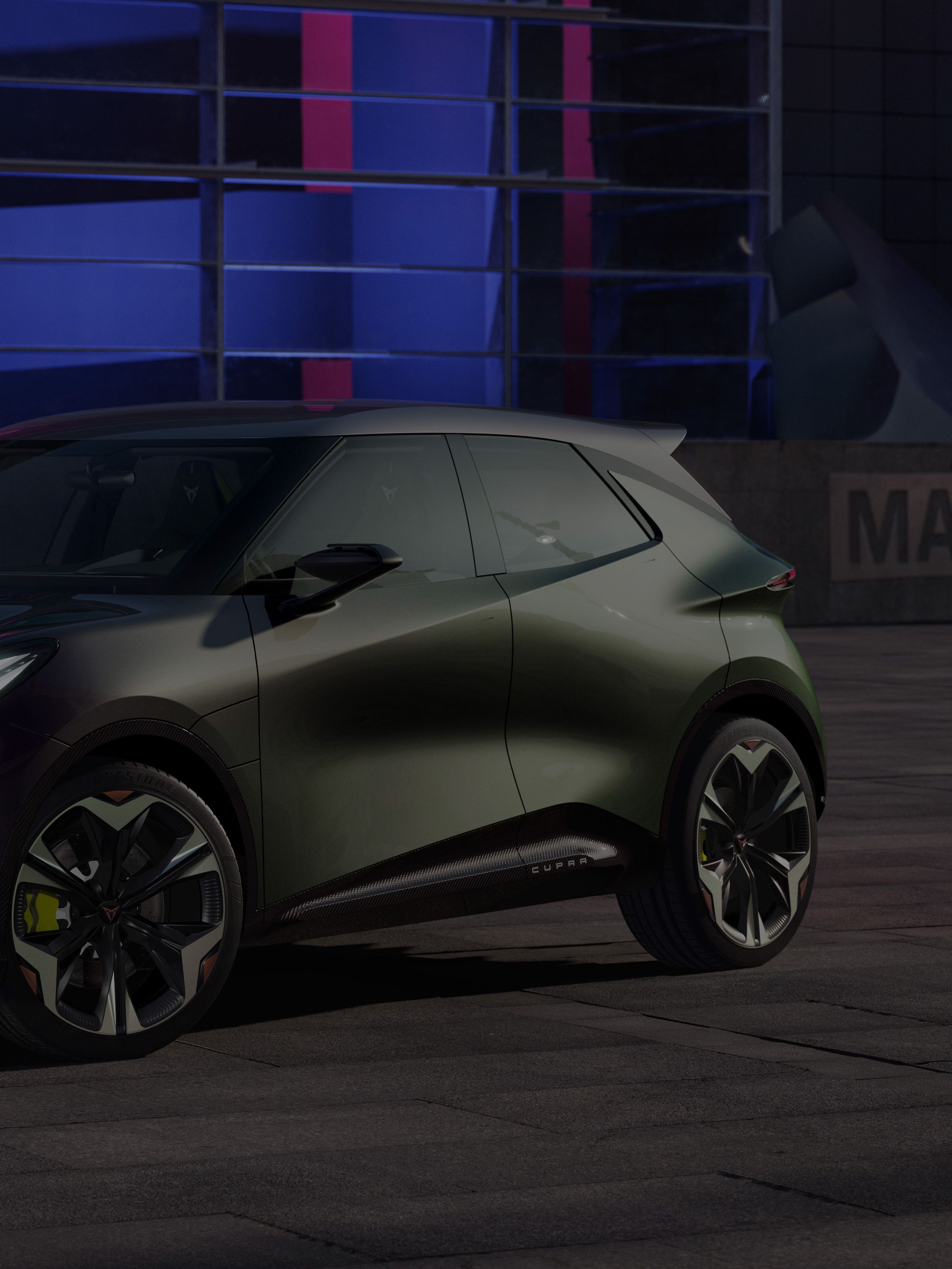 Sodobni kompaktni avtomobil CUPRA Raval je parkiran na mestnem trgu ponoči. Vozilo ima športen videz in temno barvo. V ozadju je stavba, osvetljena z modro svetlobo.