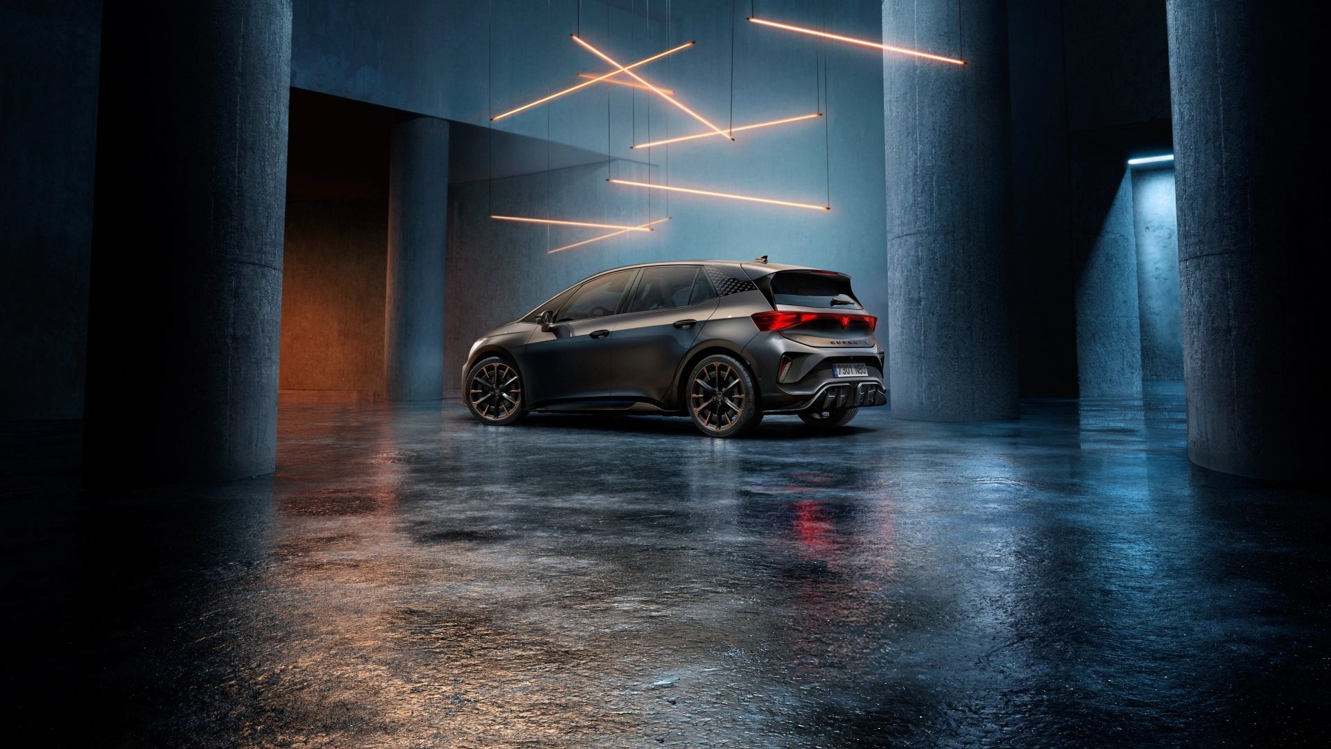 Temno siv CUPRA Born stoji v velikem industrijskem prostoru. Nad avtom visijo tanki oranžni svetlobni trakovi, ki ustvarjajo futuristično vzdušje. 