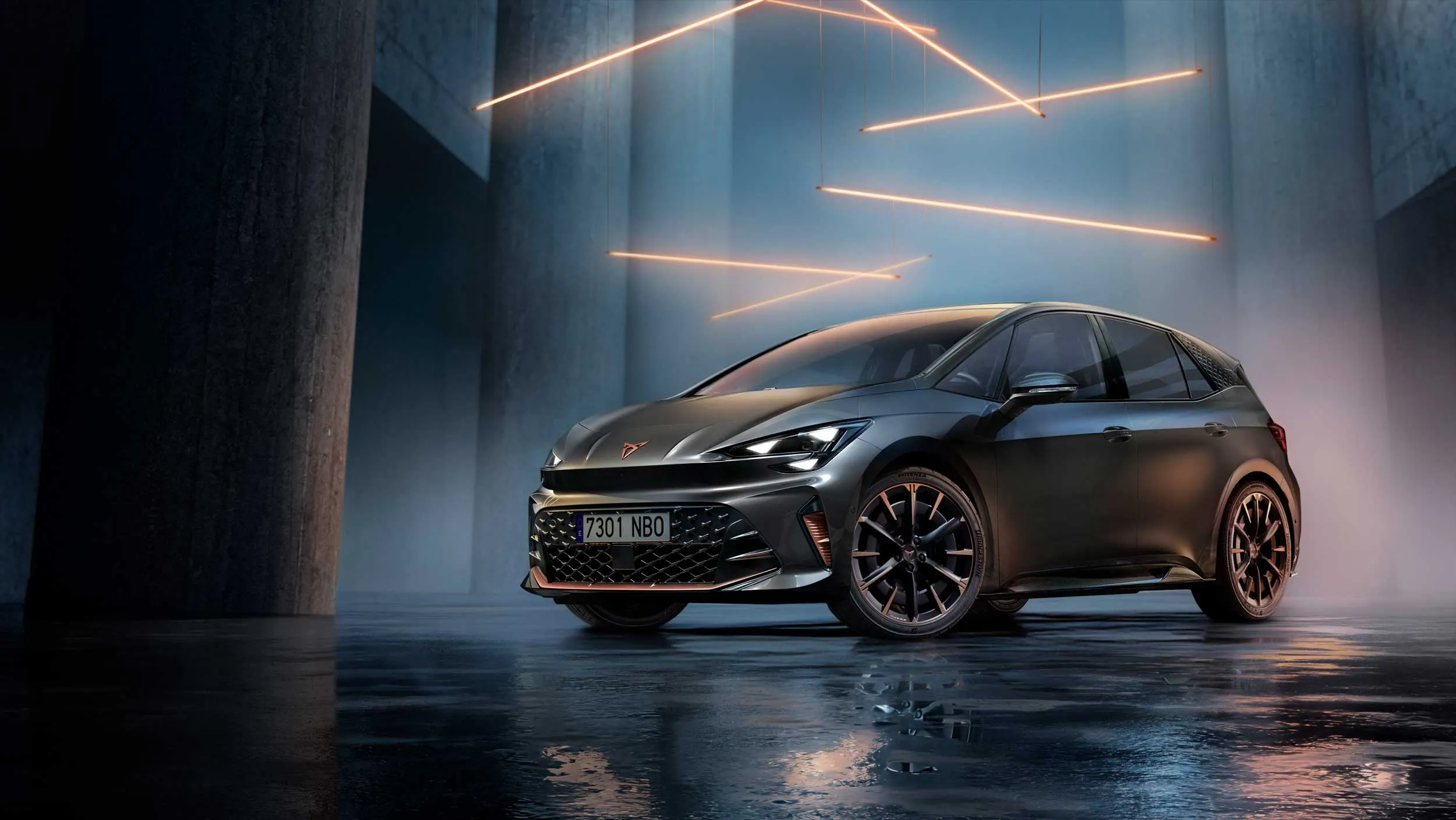 Temno siv CUPRA Born stoji v futurističnem, zatemnjenem prostoru z visokimi betonskimi stebri. Nad njim visijo tanki oranžni svetlobni trakovi, ki osvetljujejo bleščečo karoserijo in kovinska platišča. 