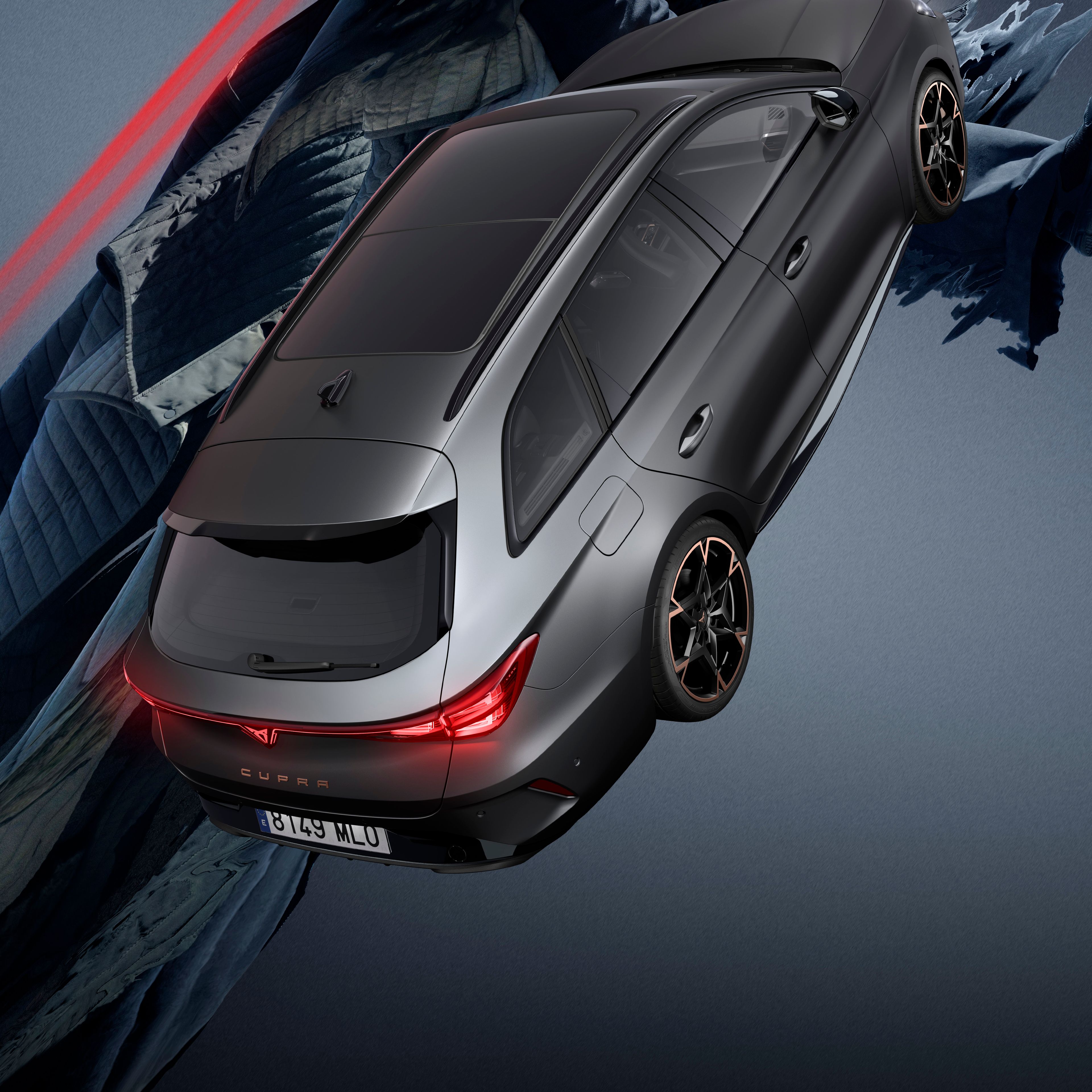 Zadnja stran avtomobila CUPRA LEON SPORTSTOURER na črnem ozadju, ki se zdi, da gre po strmem pobočju. Avtomobil ima rdeče zadnje luči in črne platišča. Za avtomobilom je figura z zamegljenim obrazom, ki drži rdeče svetlobne trakove.