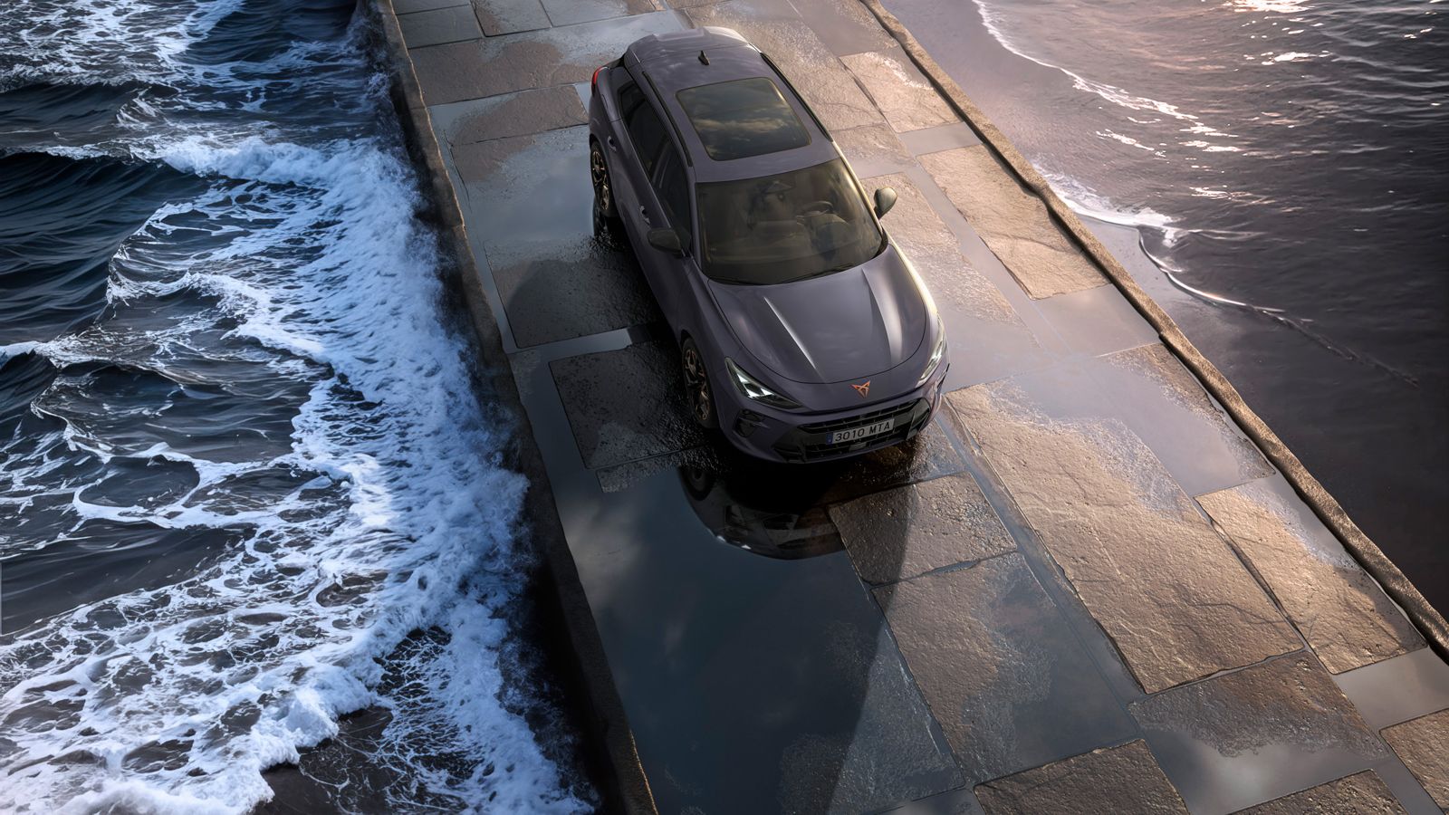 Hibridni SUV Cupra Terramar 2024 na mokrem vozišču ob morju, z elegantnimi žarometi, sodobnimi aluminijastimi platišči in animalističnim sprednjim delom.