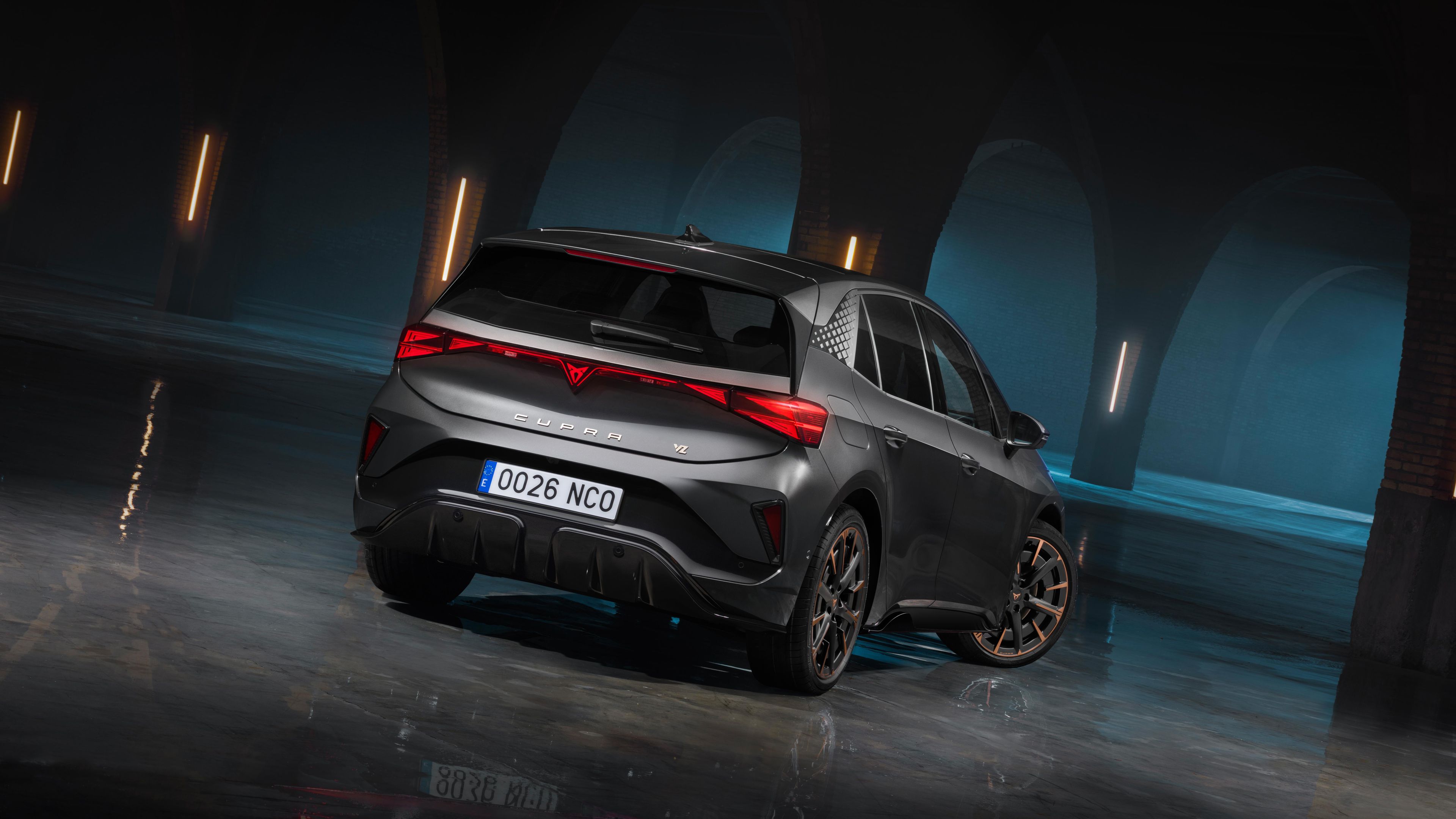 Zadnji del vozila CUPRA Born VZ v temnem prostoru z oboki in refleksijo na mokrih tleh. LED svetlobni podpis poudarja športen in sodoben dizajn.