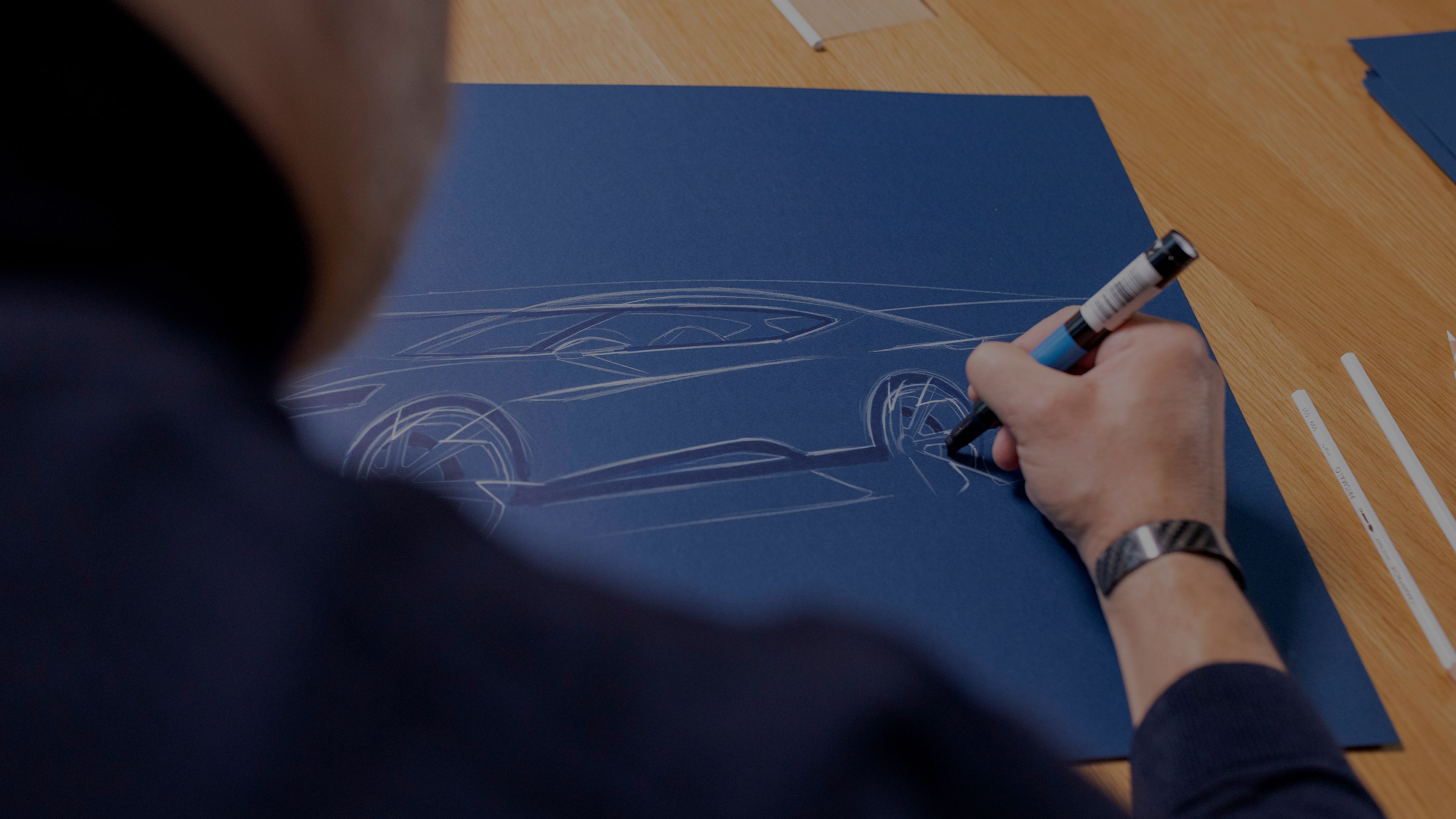 Oblikovalec riše skico avtomobila na modrem papirju. Risba prikazuje profil športnega avtomobila znamke CUPRA.