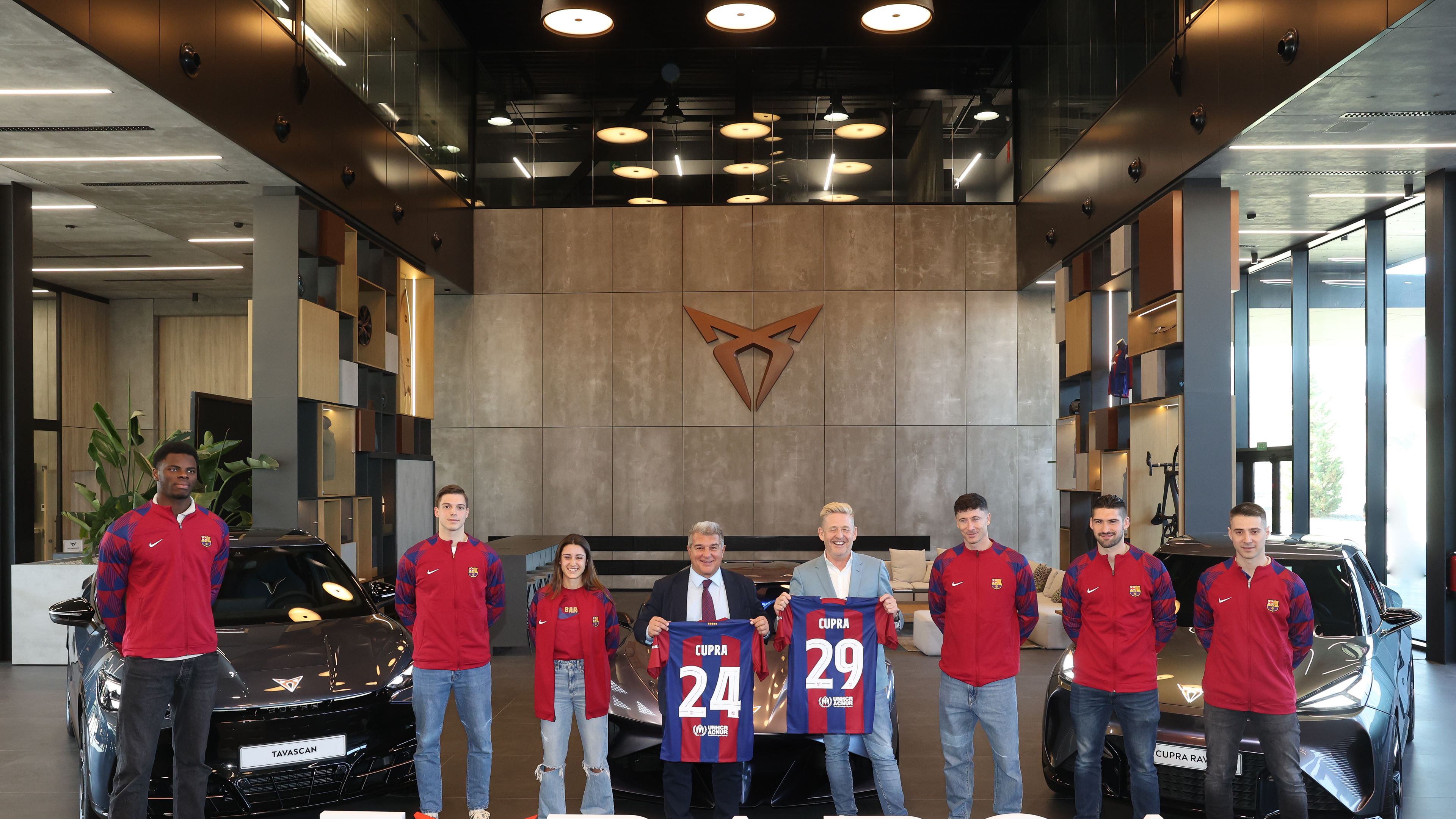 Skupina ljudi v majicah Barcelone stoji v sodobno zasnovanem prostoru. Pred njimi je napis »I love BARÇA«, pri čemer je simbol za »love« oblikovan iz logotipa znamke CUPRA. V ozadju so parkirana tri vozila CUPRA.