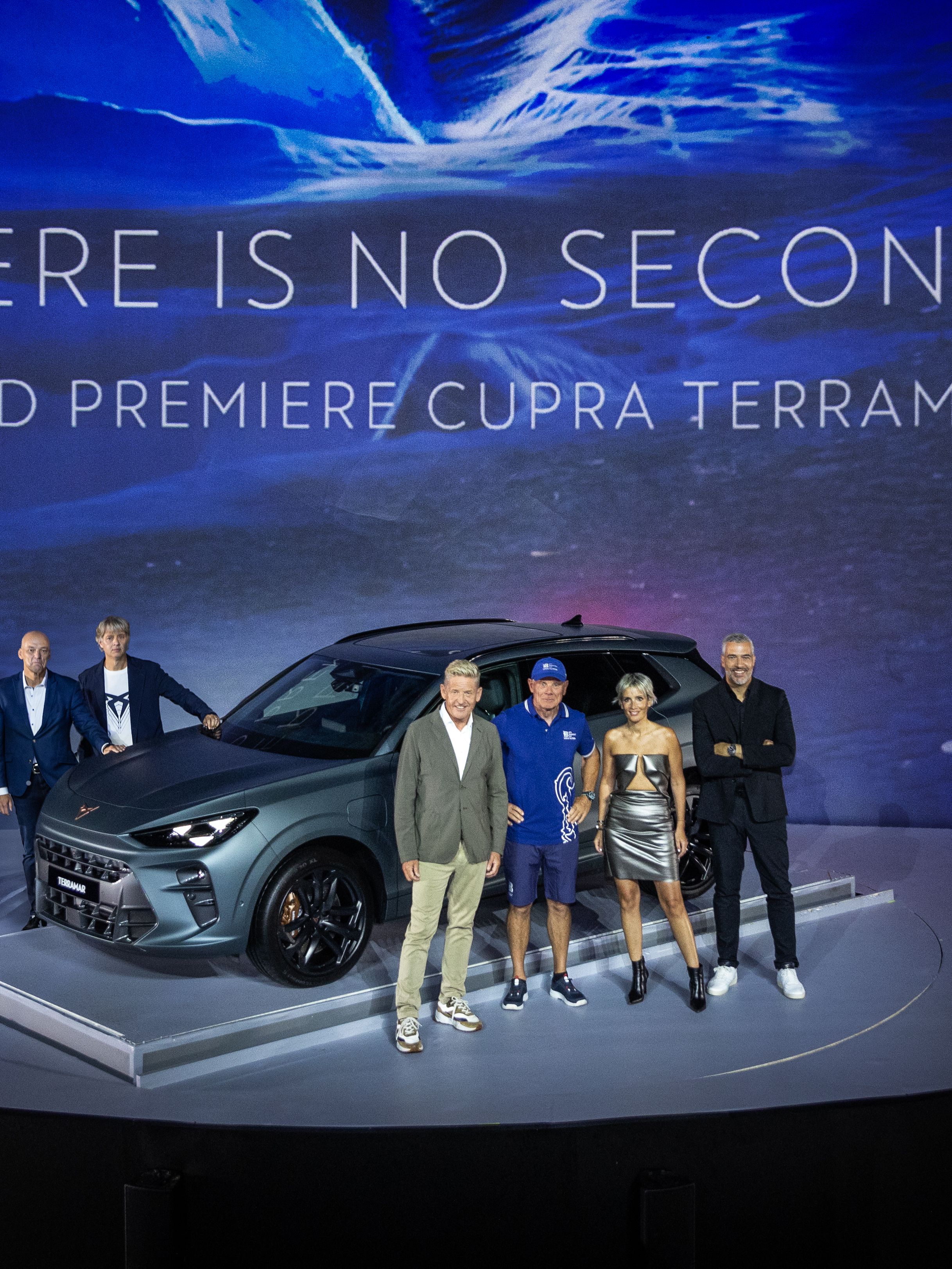 Na sliki je skupina ljudi, ki stojijo pred novim avtomobilom Cupra Terramar na svetovni premieri. Ozadje prikazuje modro osvetljeno grafiko z napisom "THERE IS NO SECOND world premiere CUPRA Terramar". 
