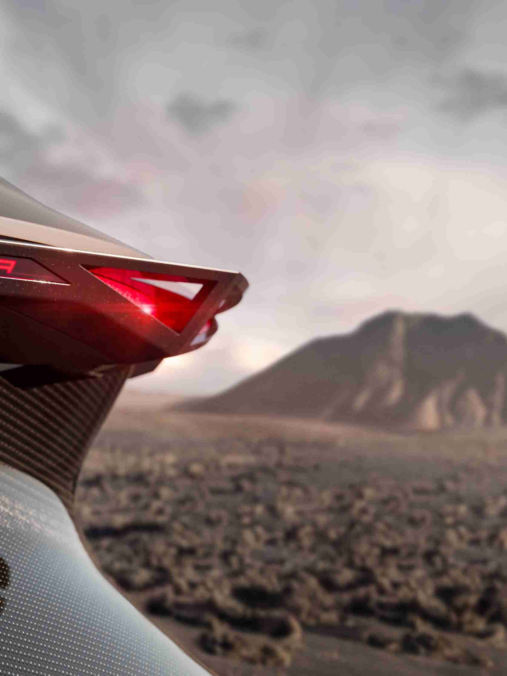 Detail avtomobila znamke CUPRA prikazuje zadnjo desno luč z rdečim svetlobnim trakom in napisom "TINDRAYA". V ozadju je vulkanska pokrajina z goro in kamnitim terenom.