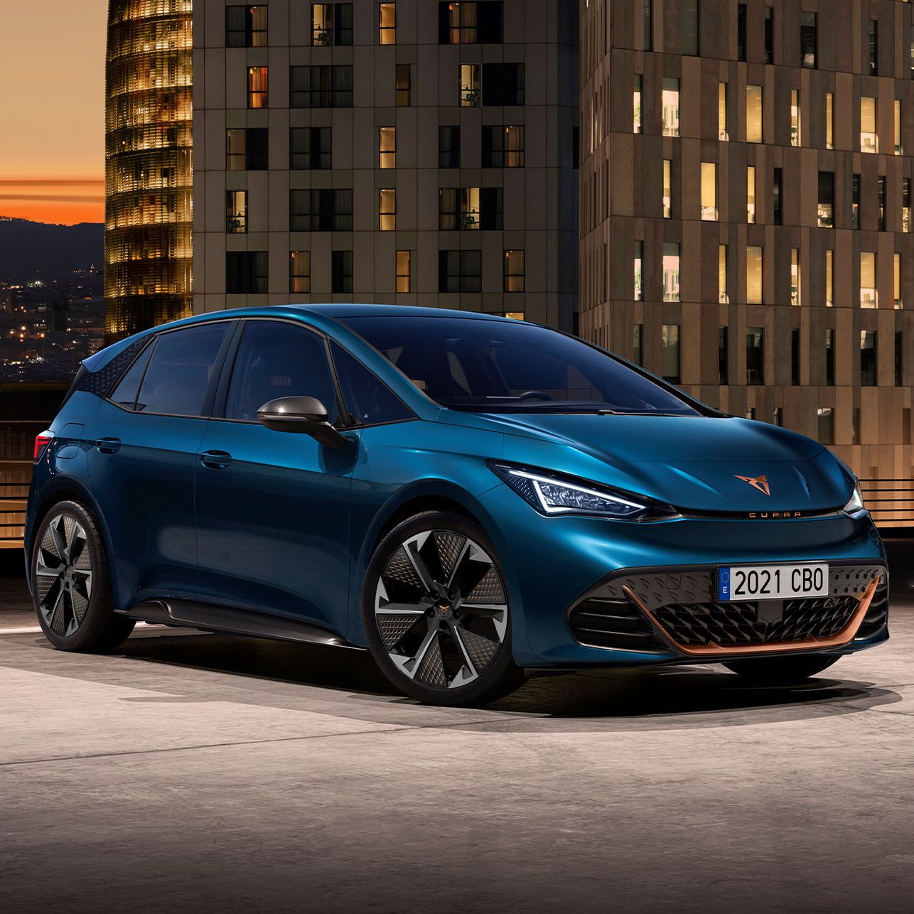 Na sliki je električni avtomobil Cupra Born na strehi parkirišča v mestnem okolju ob sončnem zahodu. Avtomobil ima modern dizajn in modro barvo, ob njem pa je logotip Euro NCAP z oceno petih zvezdic za leto 2021.