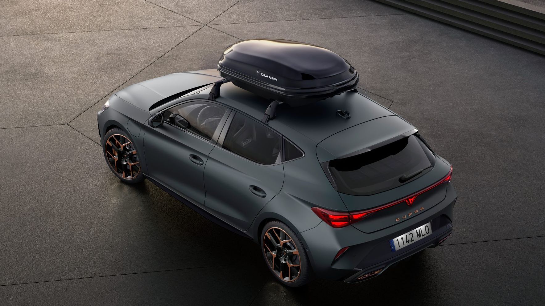 Sivi avtomobil CUPRA Leon PA, parkiran na betonski površini, ima na strehi kovček za shranjevanje.