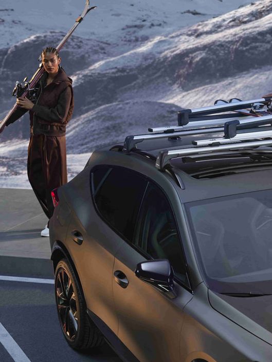 Zraven avtomobila CUPRA Formentor PA so tri ženske; dve držita smuči, ena pa jih namešča na strešni nosilec za smuči.