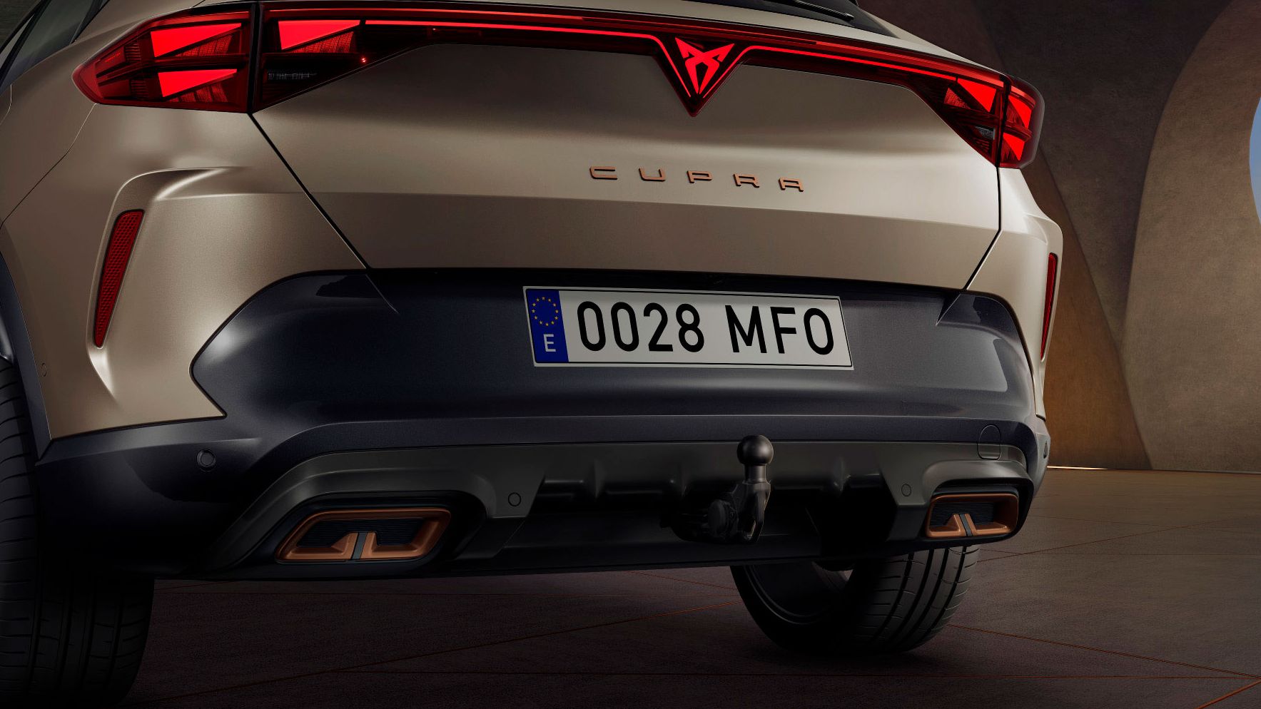 Zadnji del svetlo rjavega avtomobila CUPRA Formentor PA, s prikolico, registrsko tablico in rdečimi zadnjimi lučmi. Automobil je parkiran na betonskem podu v industrijskem prostoru.