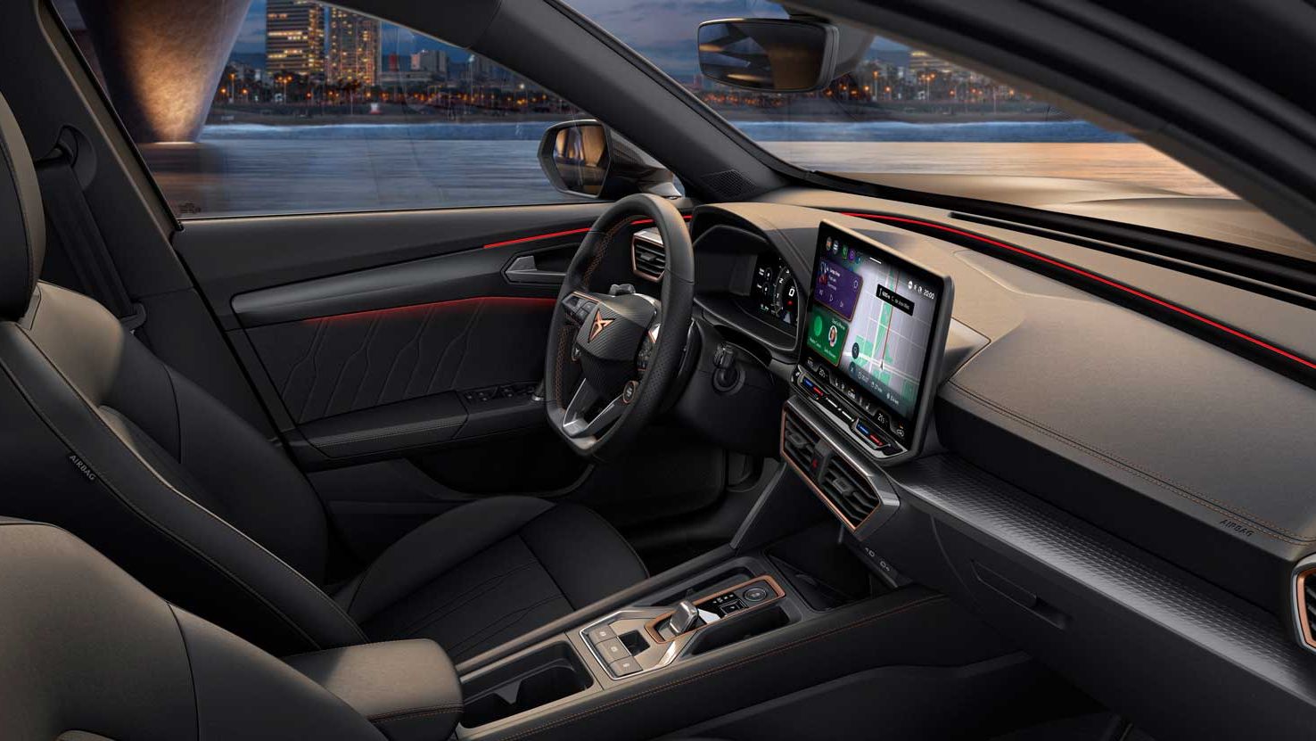 Notranjost sodobnega vozila CUPRA Formentor z velikim zaslonom infotainment sistema, volanom in upravljalnimi elementi. Vozilo ima elegantne črne sedeže, skozi okna pa se vidi osvetljeno mesto.