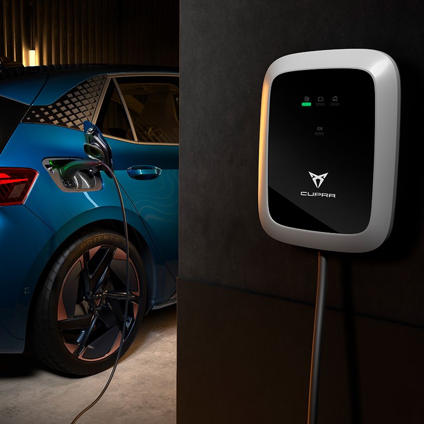Moder CUPRA Born, priključen na polnilno postajo v garaži. Polnilna postaja ima zaslon in logotip blagovne znamke CUPRA. 