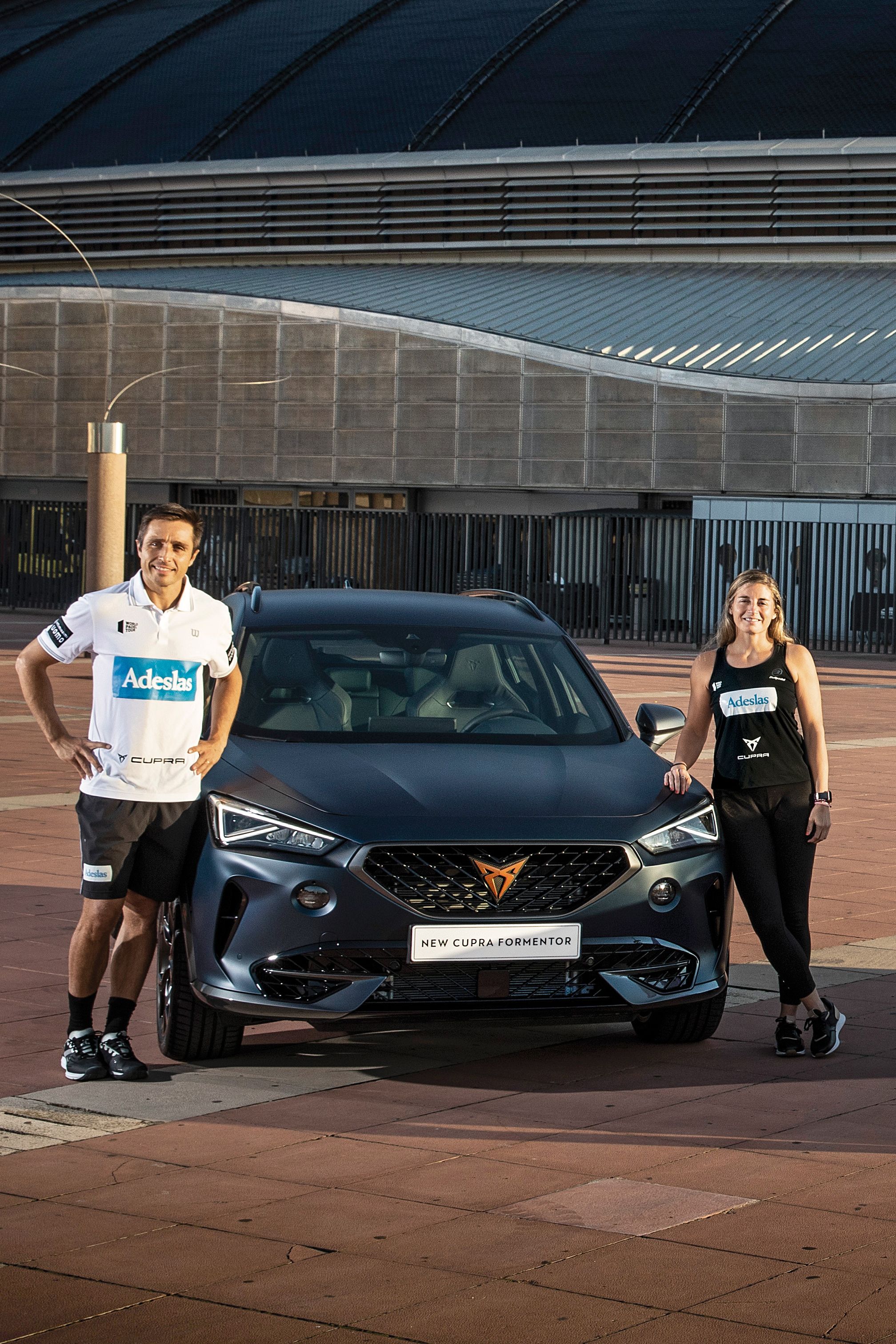 Pet igralcev padel tenisa stoji pred dvema CUPRA avtomobiloma.Za njimi je velika moderna stavba s kupolsko streho.