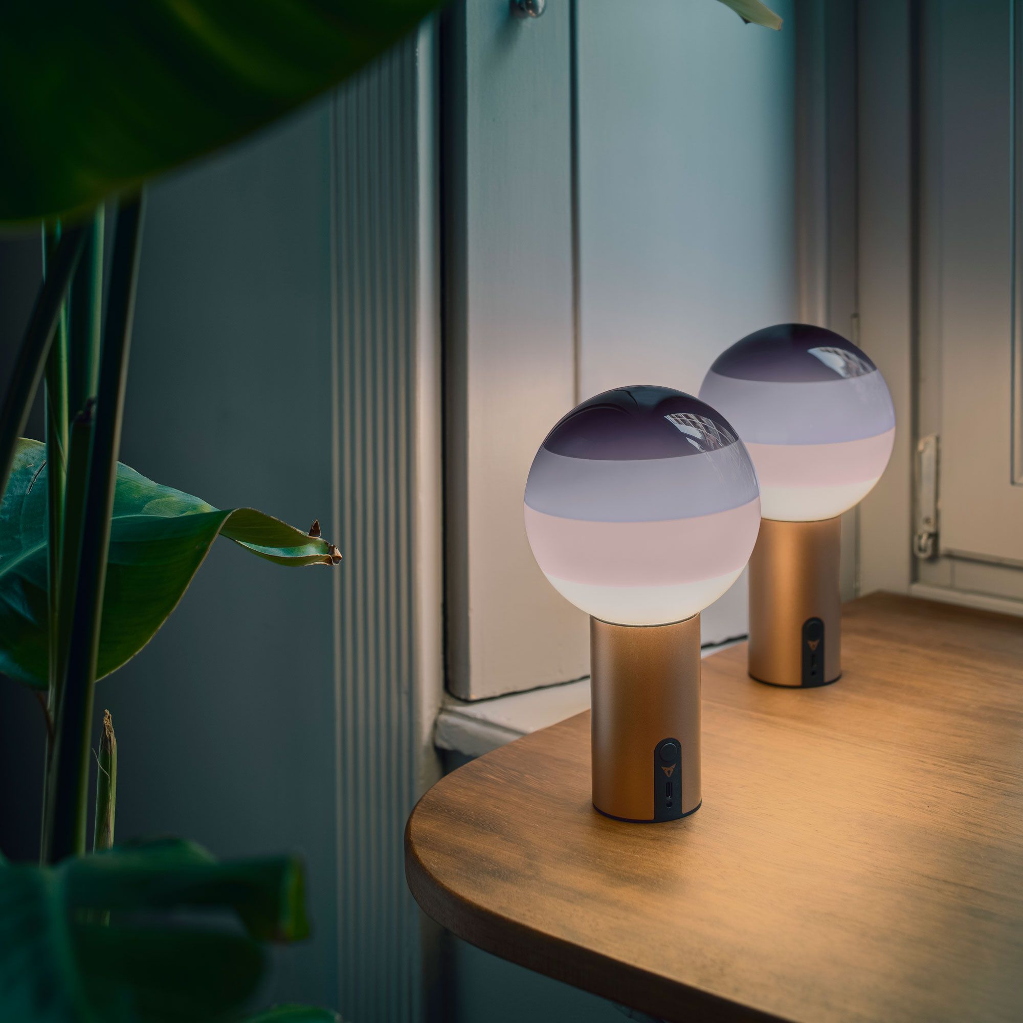 Na lesenem pultu ob oknu stojita dve namizni svetilki z okroglim senčnikom. Svetilka ima zlat podstavek z logotipom znamke CUPRA in oddaja mehko svetlobo.