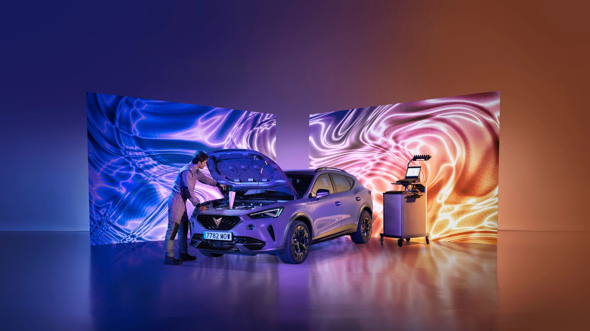 Vozilo CUPRA je pod močno osvetlitevjo v prostoru, z dvignjenim pokrovom motorja. Serviser popravlja prednji del vozila.