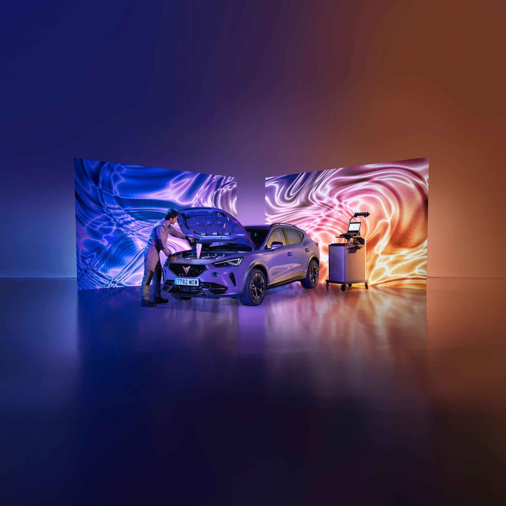 Vozilo CUPRA je pod močno osvetlitevjo v prostoru, z dvignjenim pokrovom motorja. Serviser popravlja prednji del vozila.