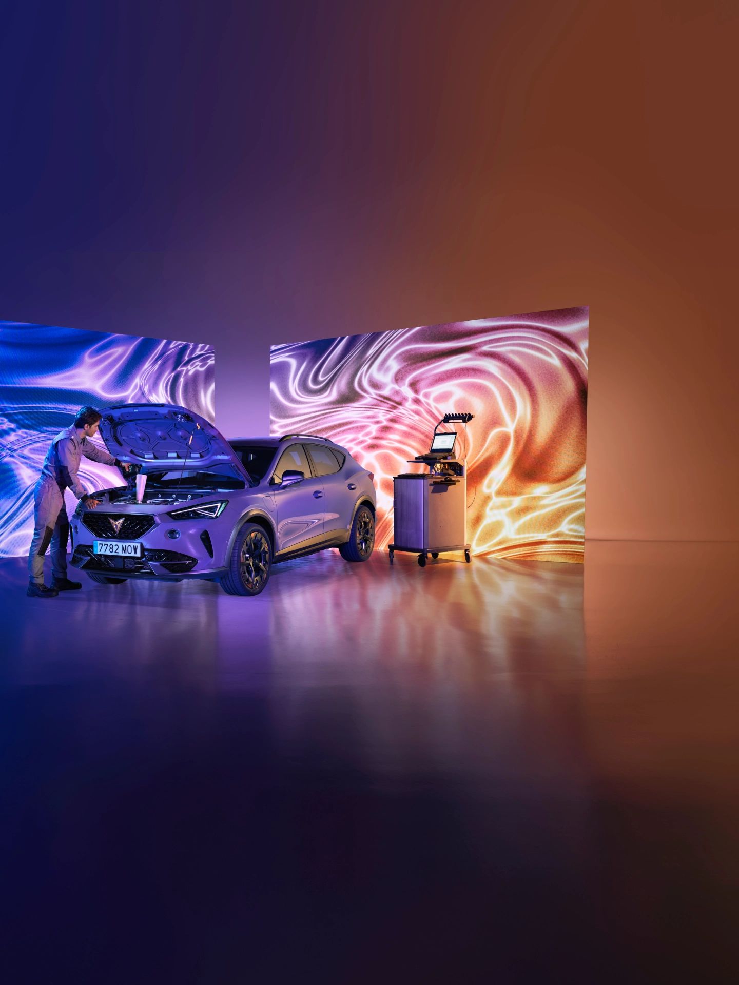 Vozilo CUPRA je pod močno osvetlitevjo v prostoru, z dvignjenim pokrovom motorja. Serviser popravlja prednji del vozila.