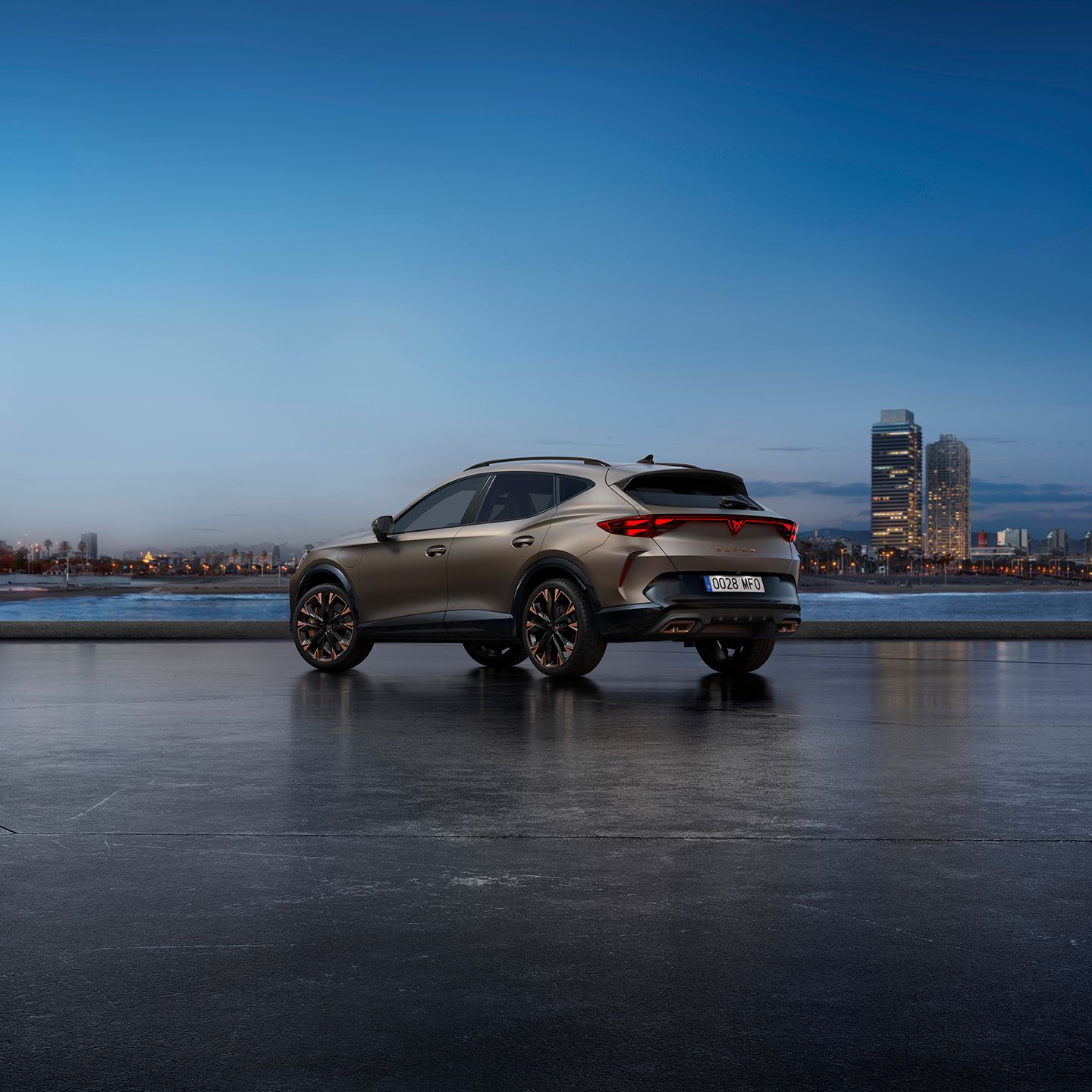 Na sliki je bronasti avtomobil CUPRA Formentor parkiran ob vodni gladini s mestno panoramo v ozadju. V daljavi so vidni visoke stavbe in mestna svetila.