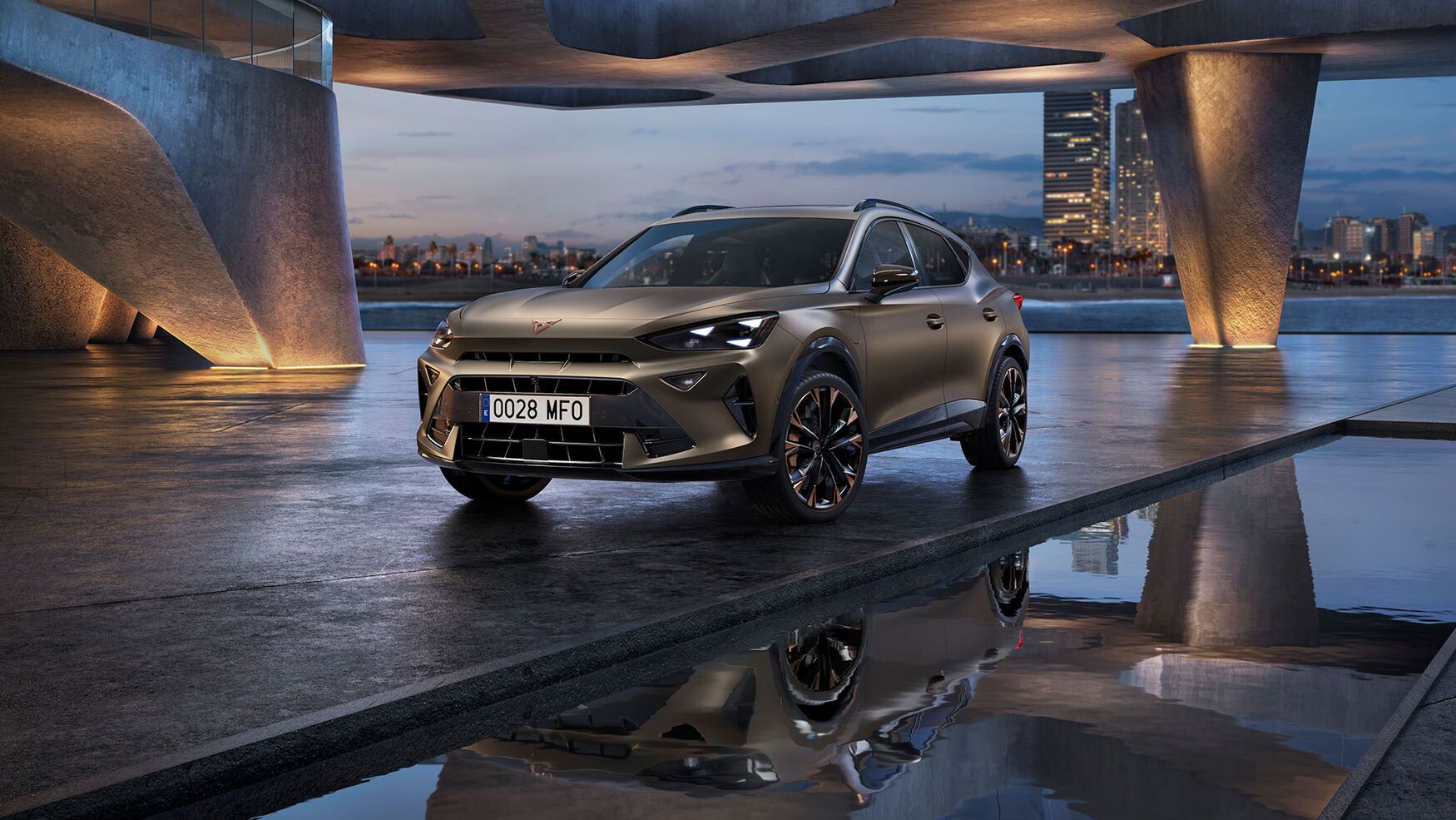 Moderen Cupra Formentor SUV je parkiran v urbanem okolju ob vodi, kjer se odraža v mirni vodi. Ozadje prikazuje mestne stavbe in visok stolp ob mestni obali v večernih urah.