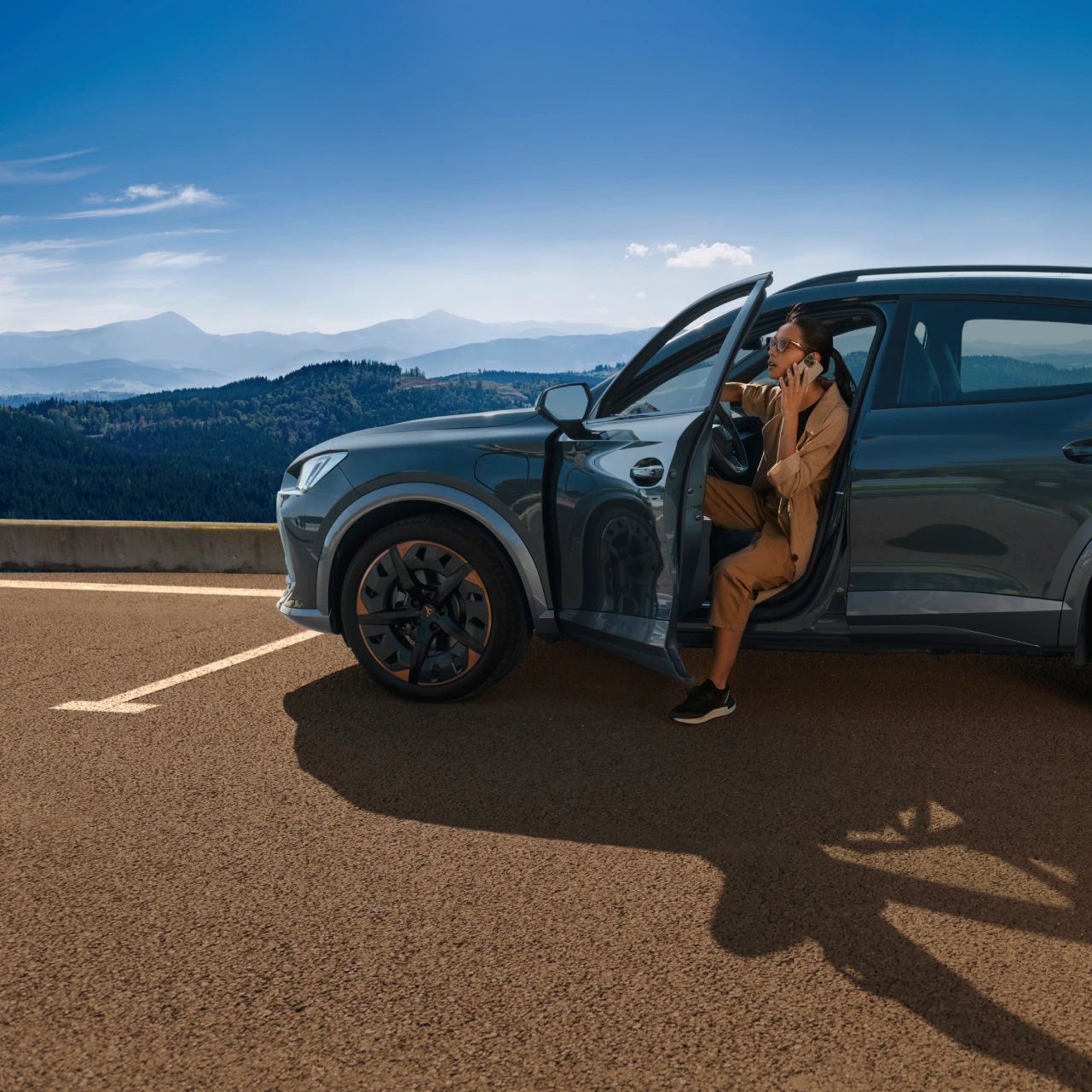 Ženska sedi v vozilu CUPRA, ki je parkiran ob cesti, z odprtimi vrati.