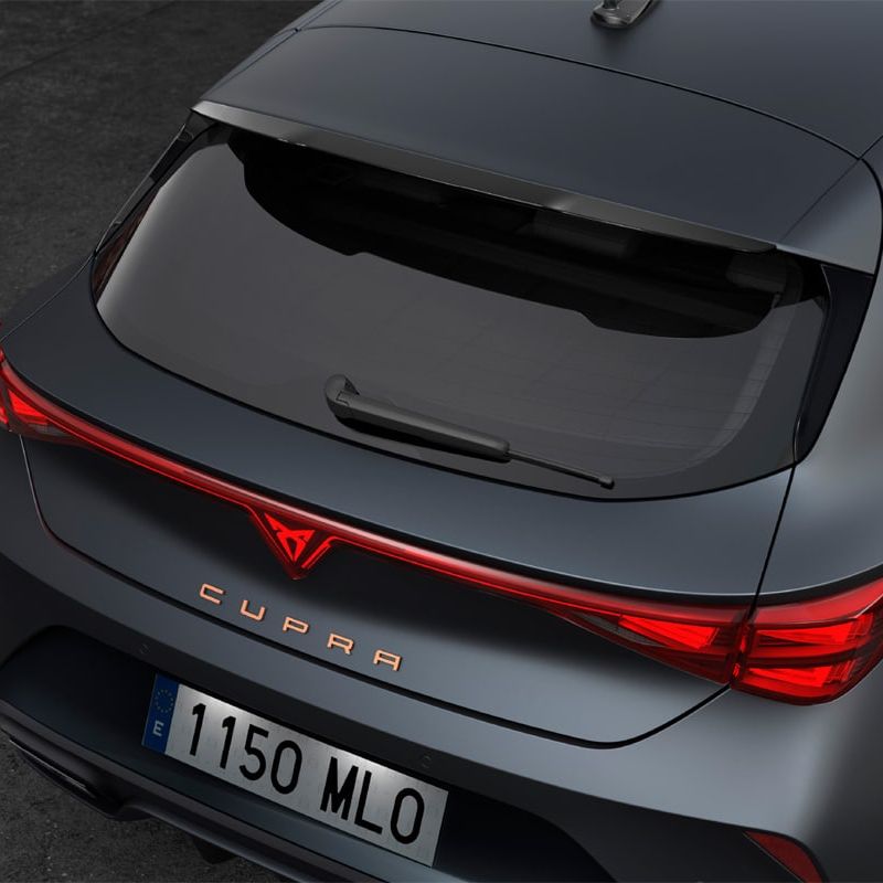 Na sliki je zadnji del sivega avtomobila CUPRA Leon PA. Avto ima tridimenzionalne zadnje luči. Osvetljena je značilna rdeča črta na spojlerju zadnjega dela.