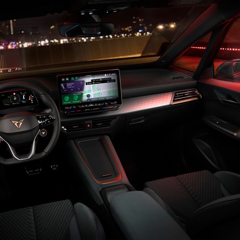 Notranjost avtomobila CUPRA BORN VZ, opremljena z osvetlitvijo in tehnologijo. Osrednji del prikazuje velik zaslon na dotik na armaturni plošči, volan ima digitalne prikazovalnike. Osvetlitev v avtomobilu je rdeča, kar daje urban in futurističen občutek.