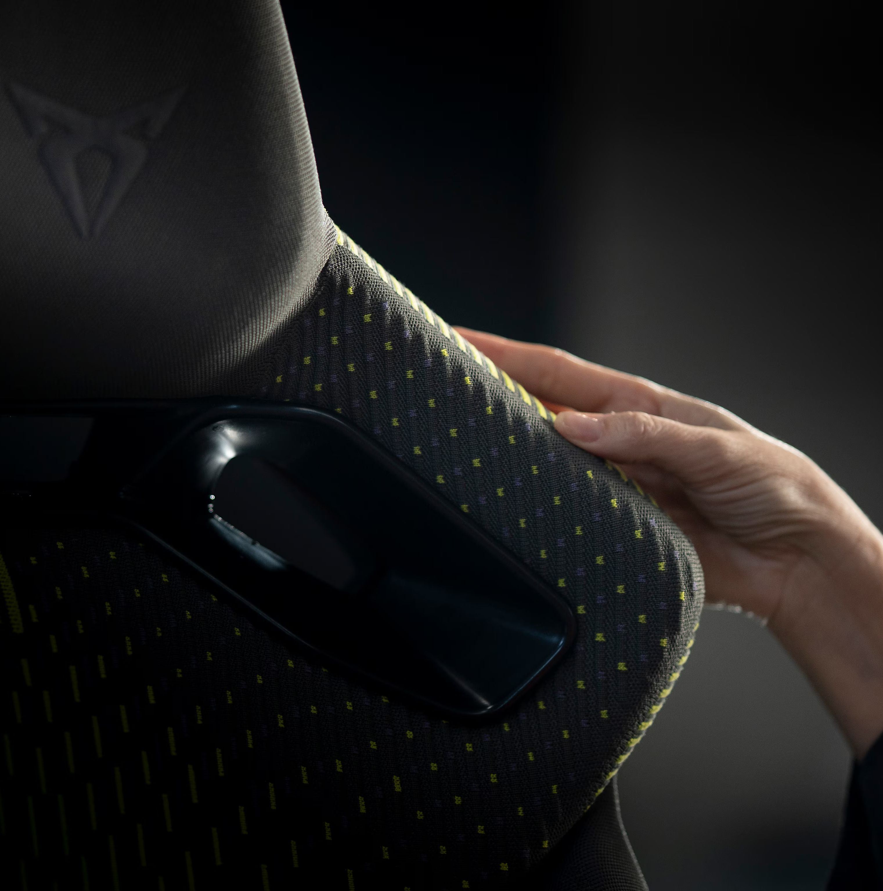 Roka se dotika tekstilnega materiala na naslonu sedeža z logotipom znamke CUPRA. Detajl poudarja strukturo tkanine, kakovost izdelave in premišljen dizajn notranjosti.