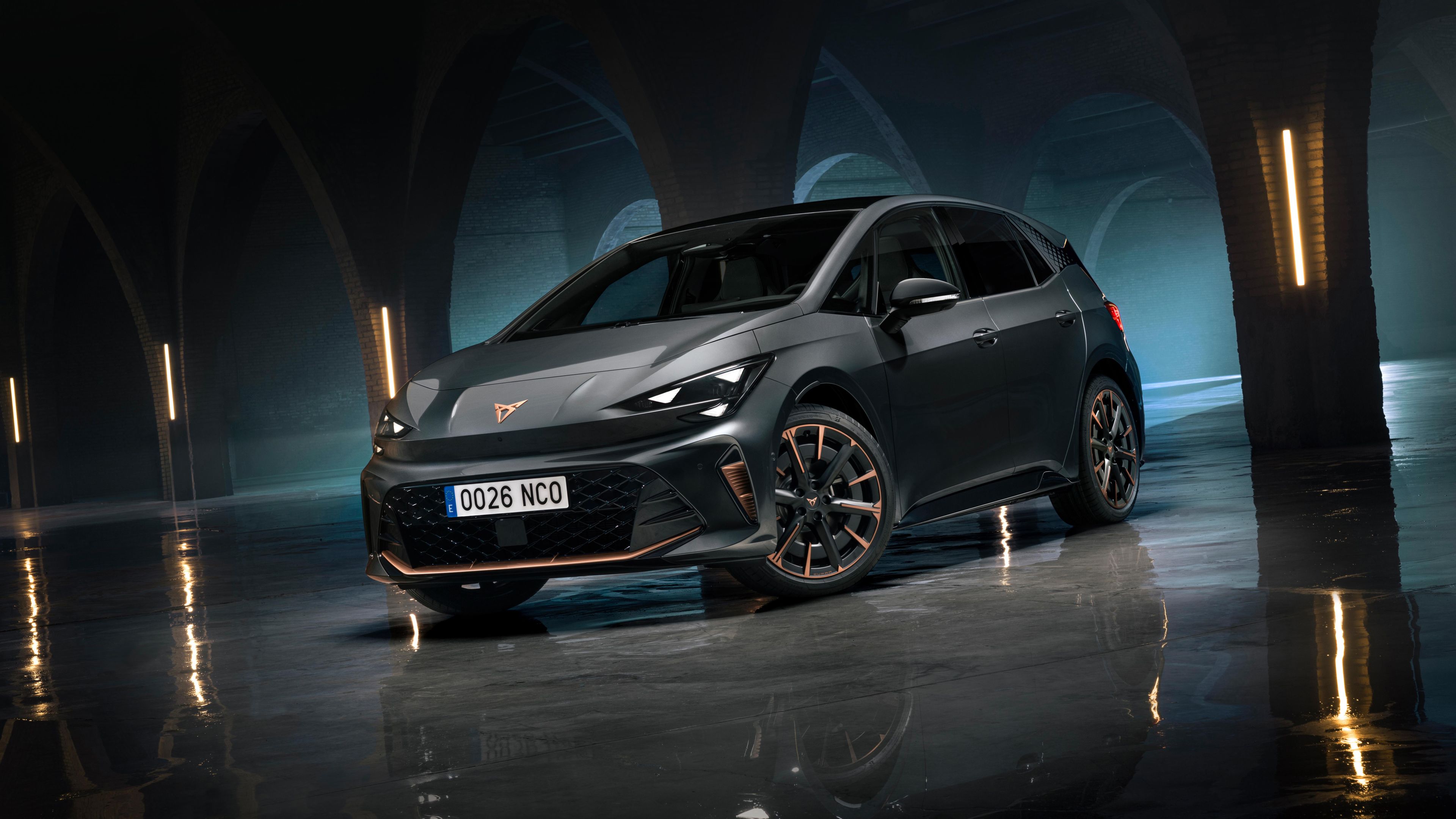 CUPRA Born stoji v temnem, arhitekturno izrazitem prostoru z oboki in refleksijo na mokrih tleh. Dramatična osvetlitev poudarja športen dizajn in električni značaj vozila.