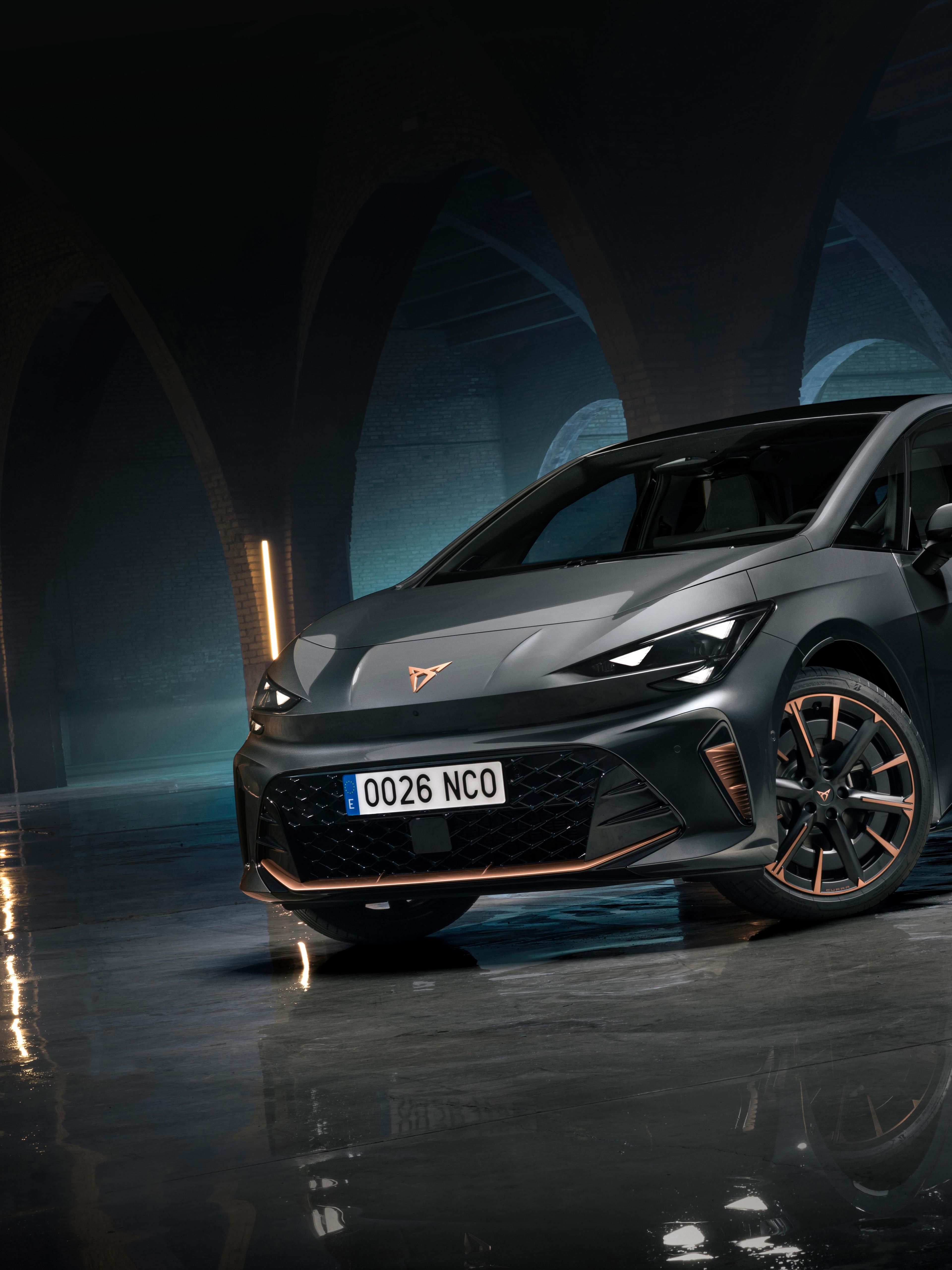 CUPRA Born stoji v temnem, arhitekturno izrazitem prostoru z oboki in refleksijo na mokrih tleh. Dramatična osvetlitev poudarja športen dizajn in električni značaj vozila.