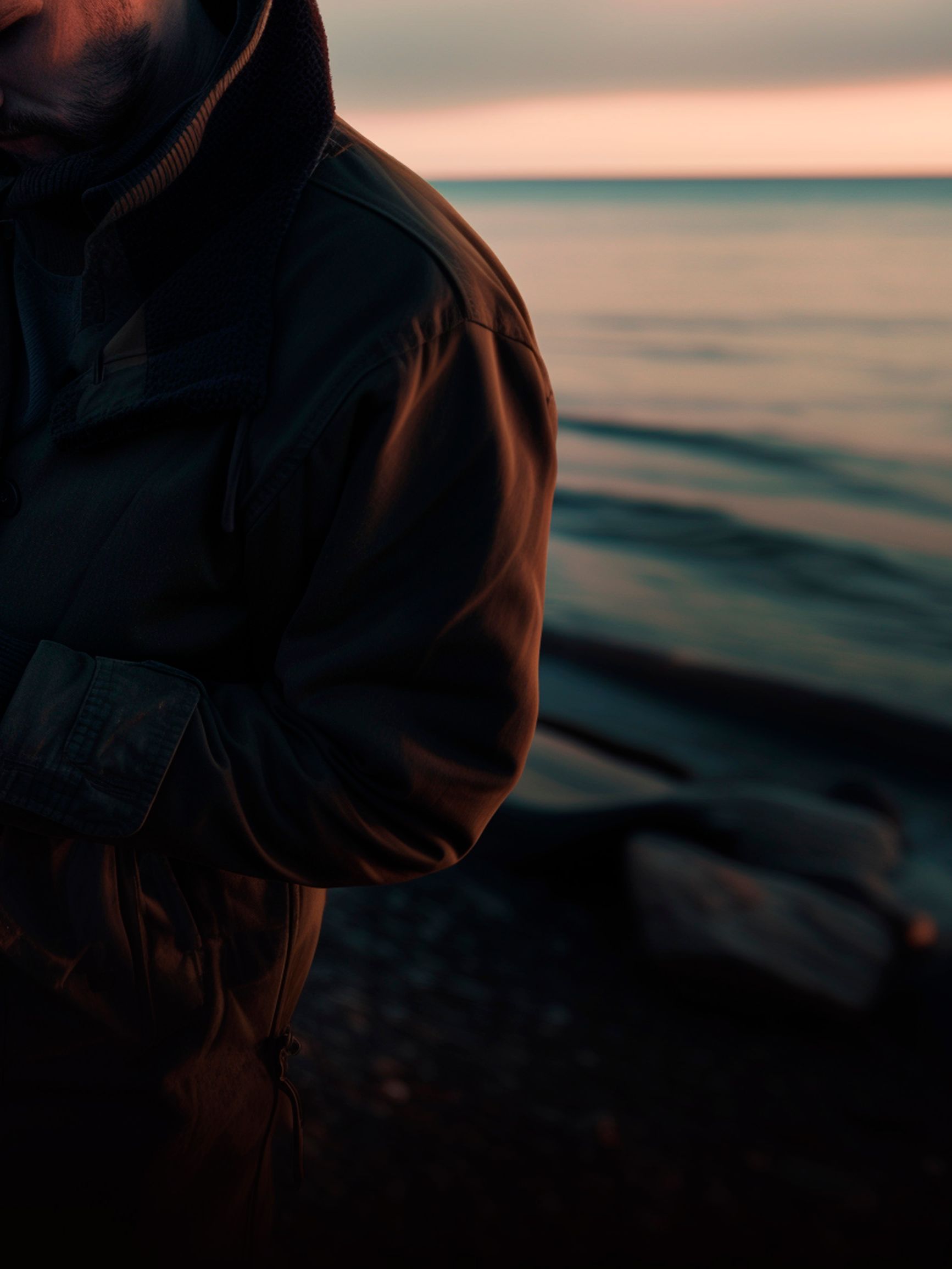 Oseba v plašču stoji na skalnati obali ob morju, v rokah drži telefon z aplikacijo CUPRA CONNECT.