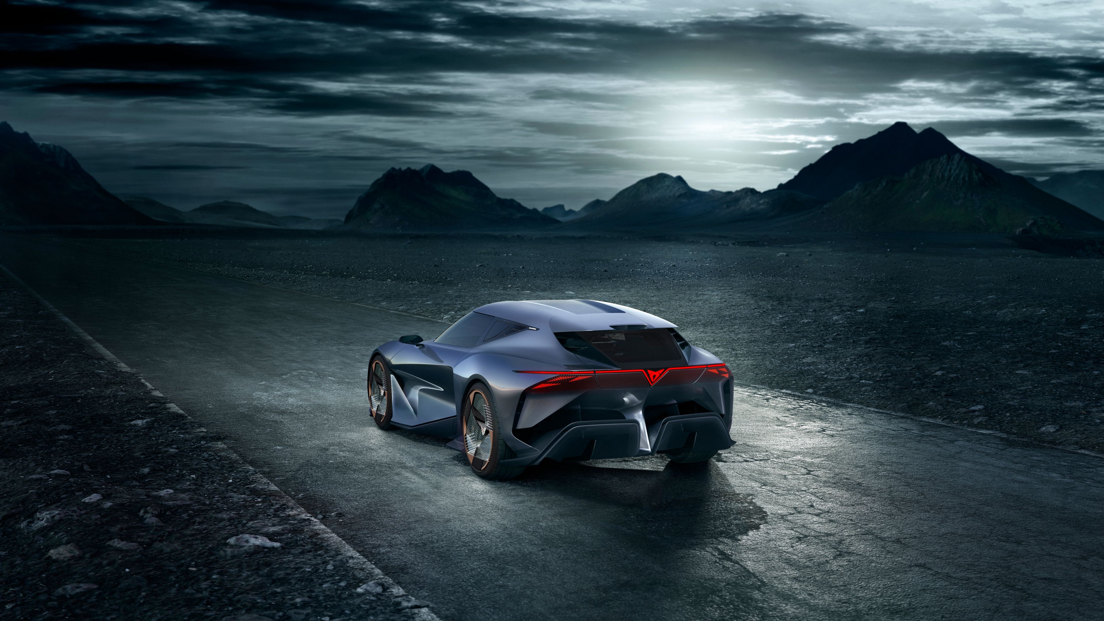 Prikaz zadnjega dela temno vijoličnega avtomobila CUPRA DarkRebel z izrazito sodobnim dizajnom. Parkiran je na cesti, nebo je temno in oblačno, v ozadju pa so vidne gore.