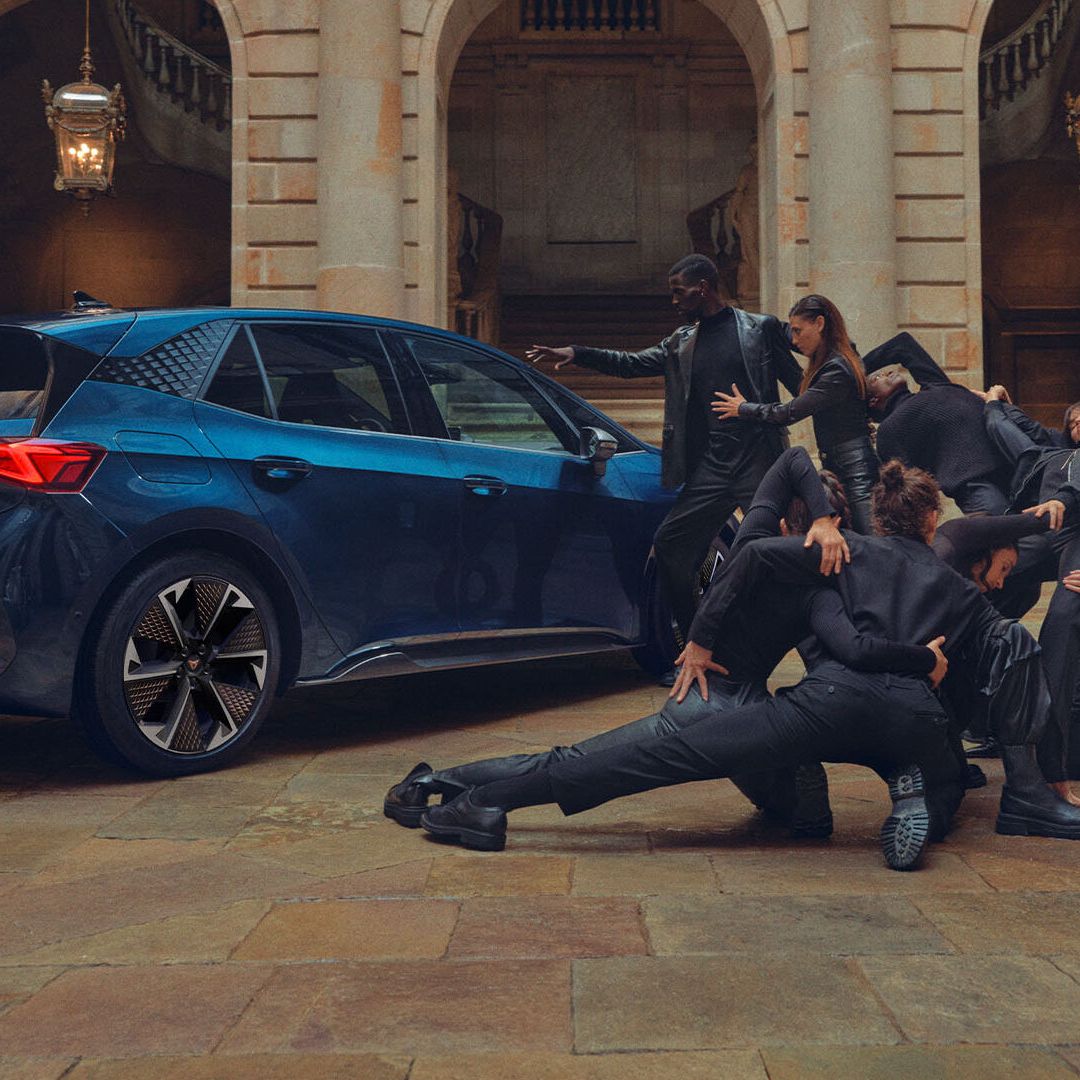 Skupina elegantno oblečenih ljudi izvaja plesne poteze poleg Cupra Borna v notranjem dvorišču zgodovinske zgradbe.