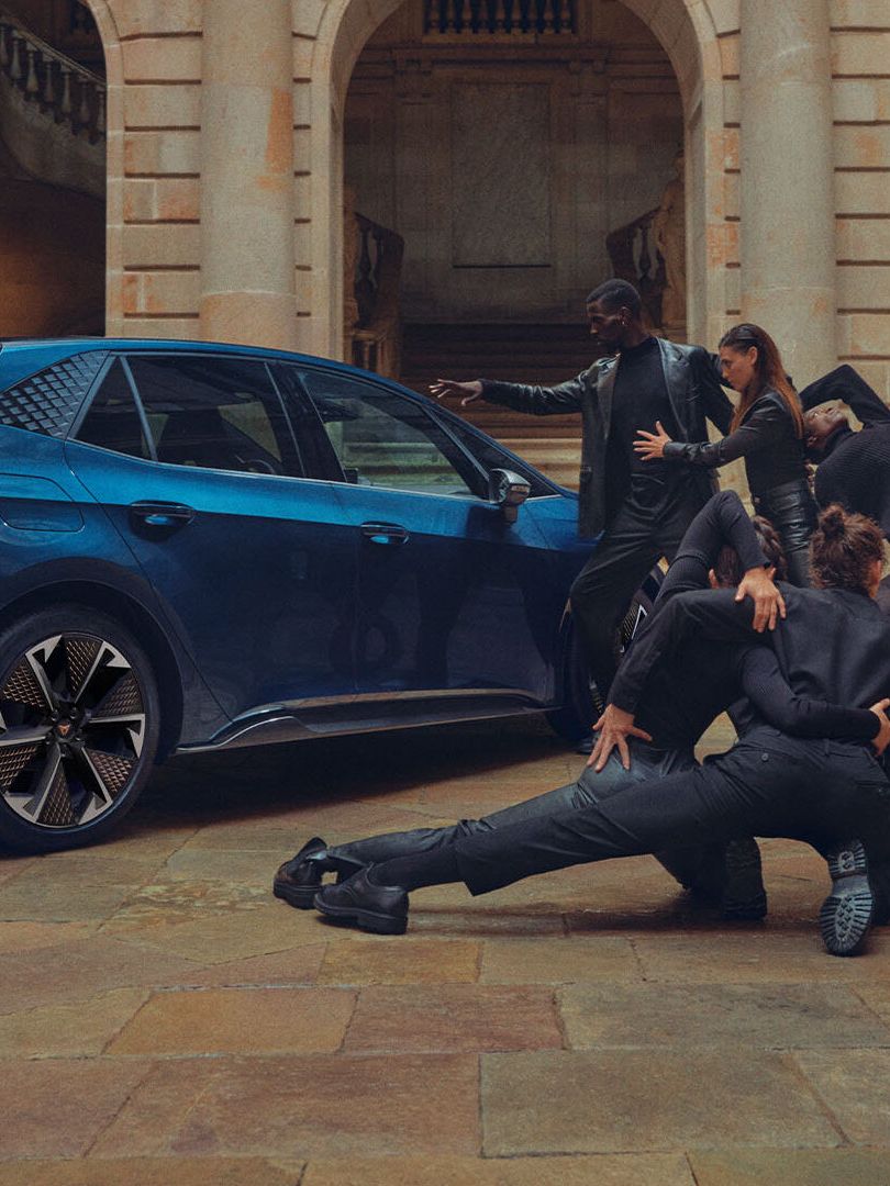 Skupina elegantno oblečenih ljudi izvaja plesne poteze poleg Cupra Borna v notranjem dvorišču zgodovinske zgradbe.