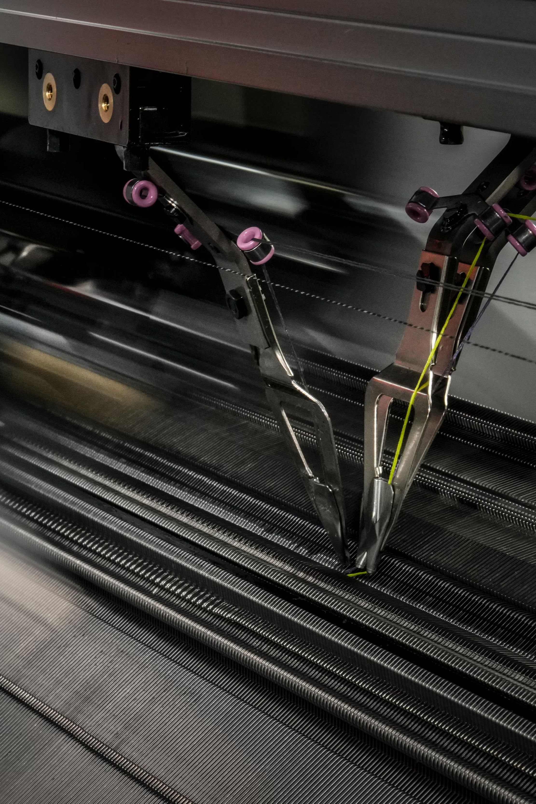 Industrijski 3D stroj v gibanju tiska oziroma plete tehnični tekstilni material. Vidni so mehanski elementi in niti, ki prikazujejo natančen proces avtomatizirane izdelave.