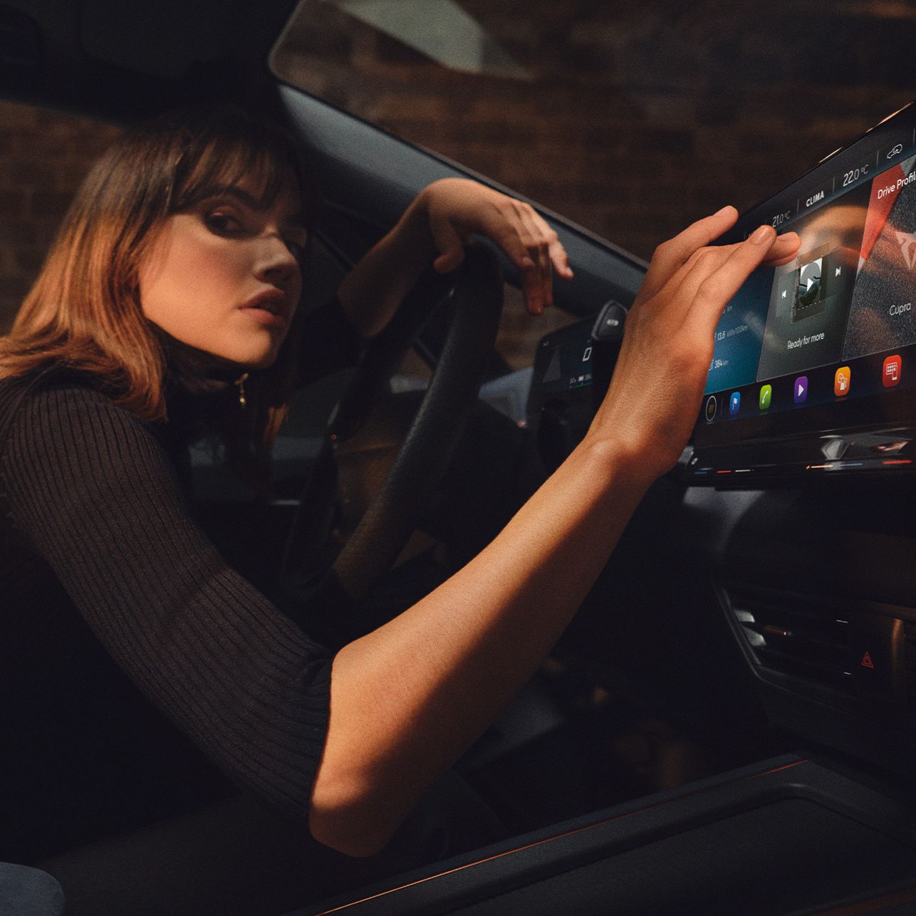 Ženska sedi za volanom avtomobila Cupra Born in upravlja z velikim zaslonom na armaturni plošči. Zaslon prikazuje različne ikone in možnosti nastavitev.