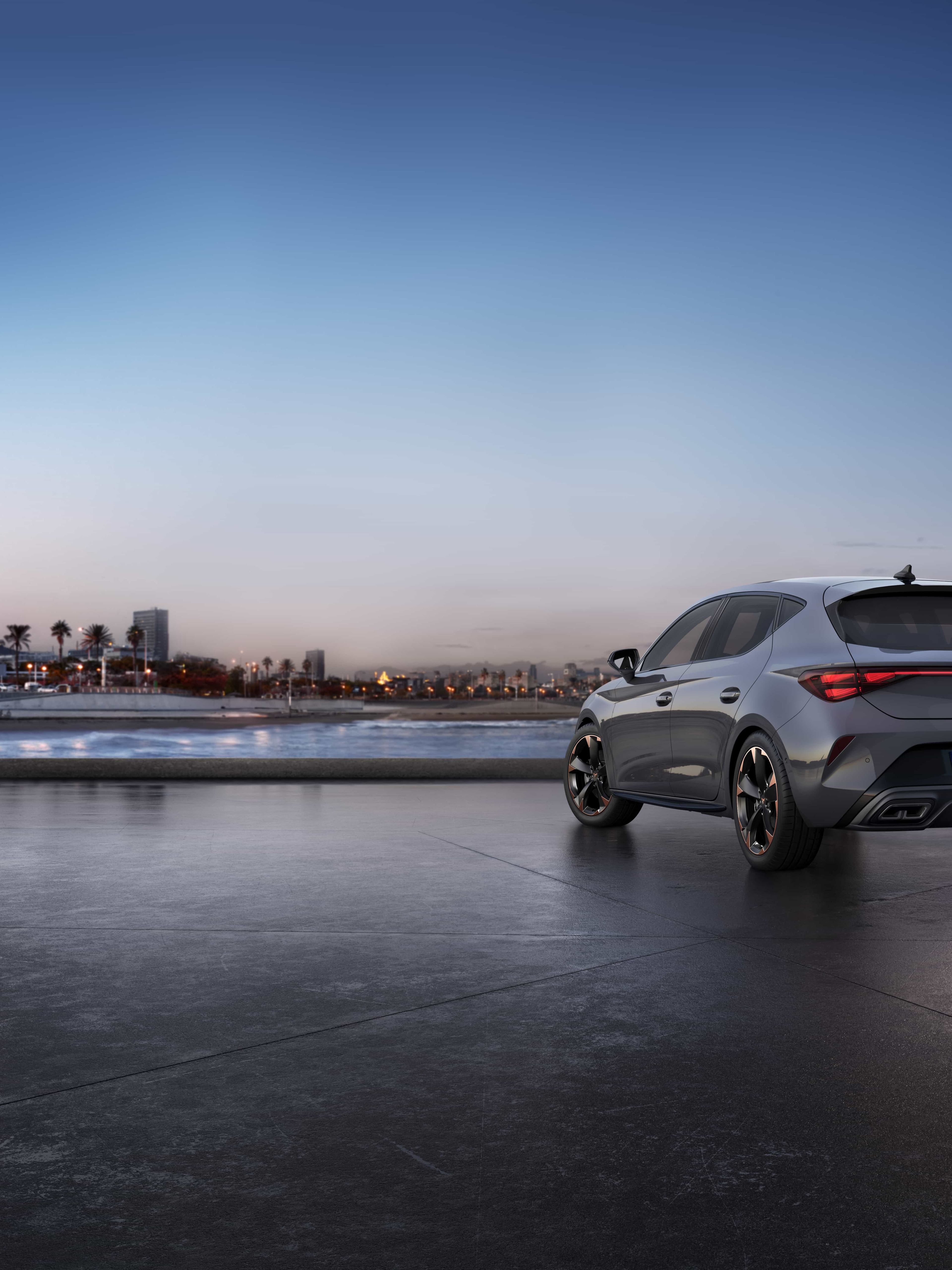 Cupra Leon je parkiran na obali ob mraku s svetlobno osvetljenimi obalnimi zgradbami v ozadju.