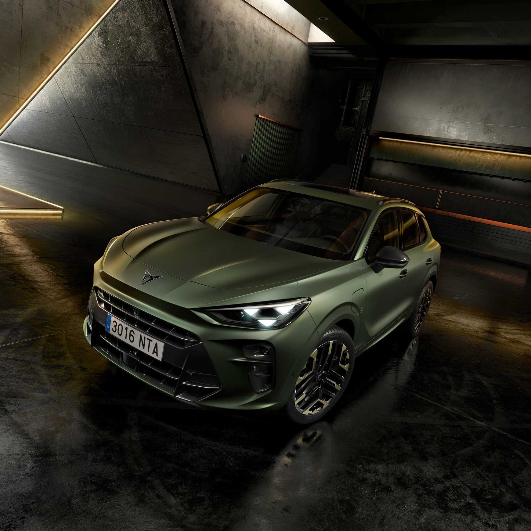Temno zelen CUPRA Terramar stoji v futuristični, zatemnjeni garaži z betonskimi stenami in odsevnimi tlemi. Avto ima ostre, agresivne linije, velik sprednji vstop za zrak in elegantna platišča. 