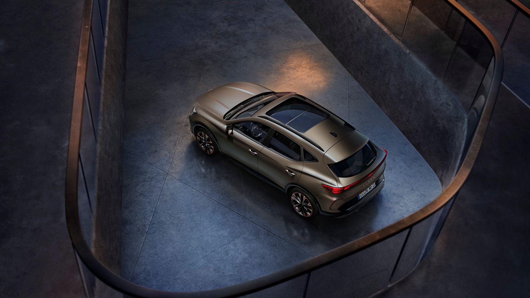 Zračno posnetek avtomobila 'CUPRA Formentor' z elegantnim dizajnom, parkiranega v sodobni zgradbi. Vozilo je zlato rjave barve.