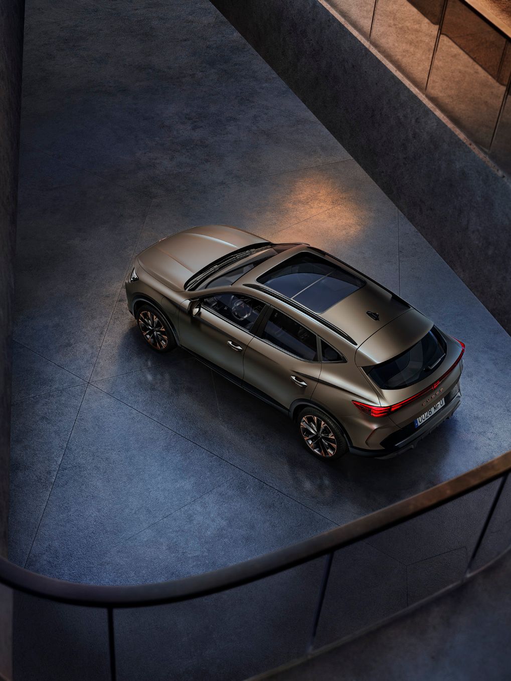 Zračno posnetek avtomobila 'CUPRA Formentor' z elegantnim dizajnom, parkiranega v sodobni zgradbi. Vozilo je zlato rjave barve.