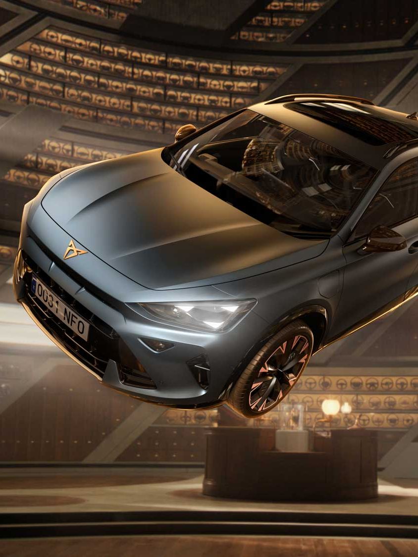 Srebrni CUPRA Formentor lebdi v futurističnem prostoru z dramatično osvetlitvijo in arhitekturnimi detajli v ozadju. V ospredju Tom Felton drži volan, prizor pa poudarja inovativen dizajn, tehnologijo in dinamičen značaj vozila.