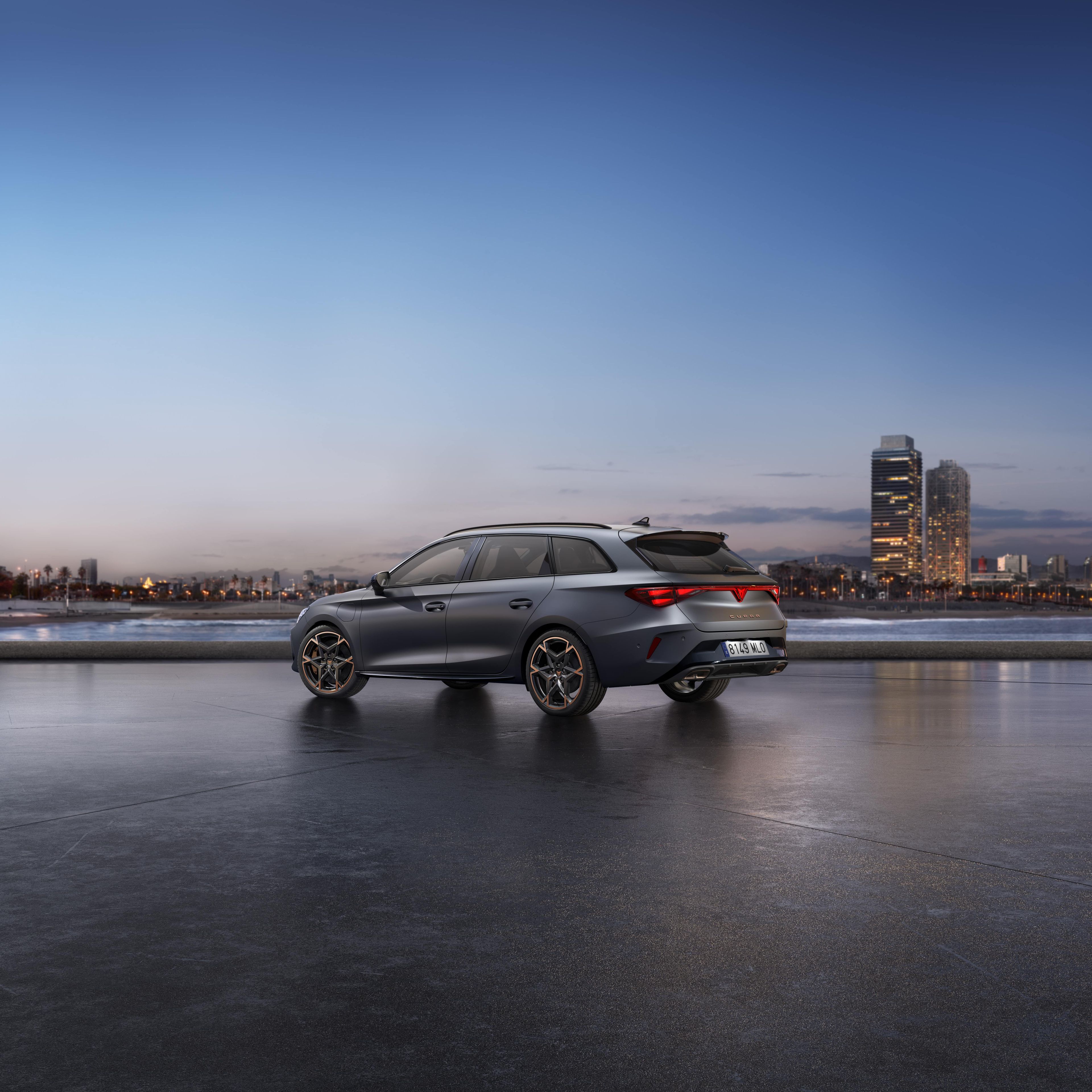 CUPRA LEON SPORTSTOURER stoji ob obali ob sončnem zahodu. V ozadju je mestno obzorje z visokimi stavbami, mokra površina pod vozilom pa odseva nebo.