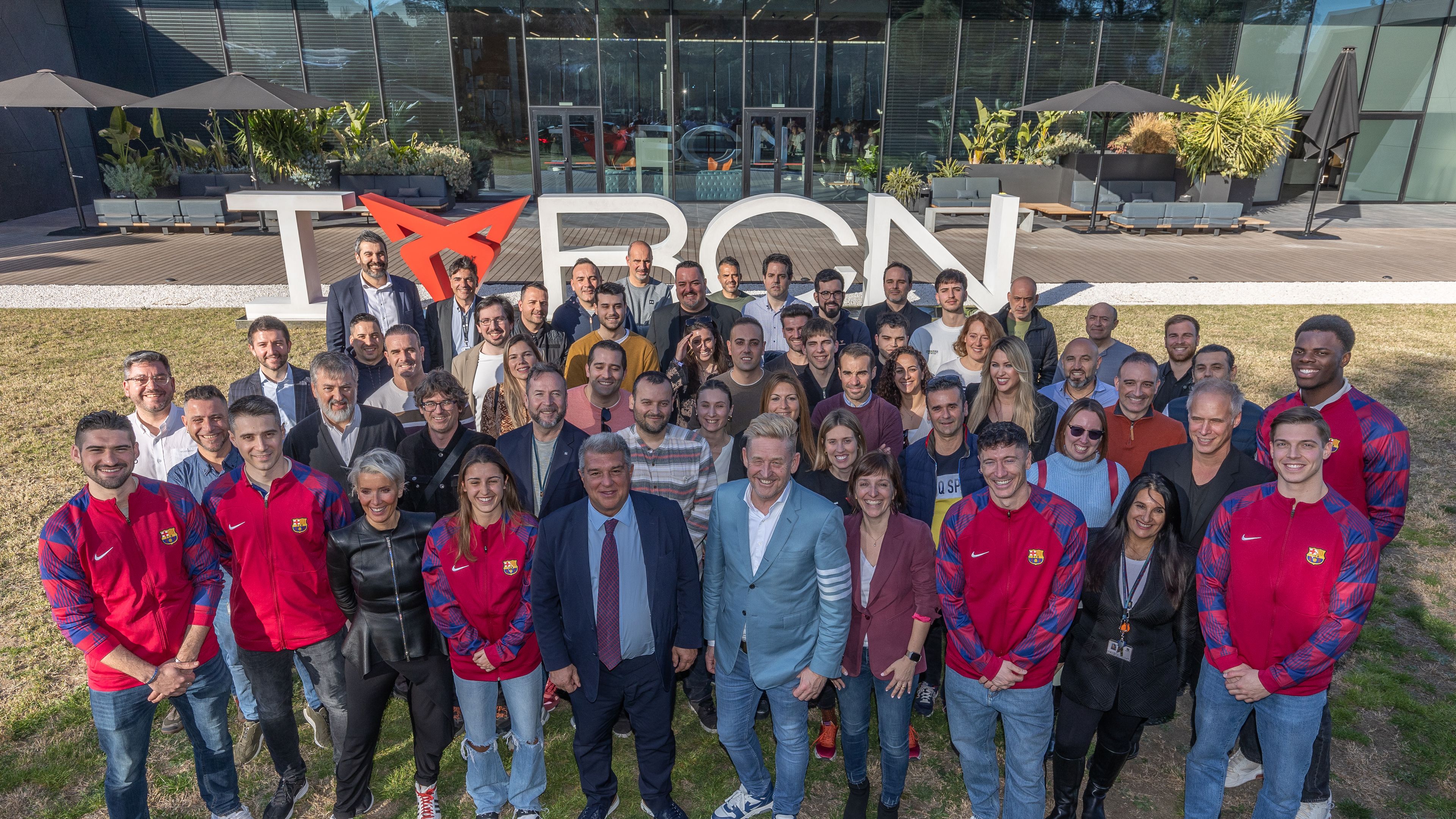 Skupina ljudi, stoji pred stavbo, z napisom »I love BARÇA«, pri čemer je simbol za »love« oblikovan iz logotipa znamke CUPRA. Ljudje so postrojeni v več vrstah in gledajo proti kameri.