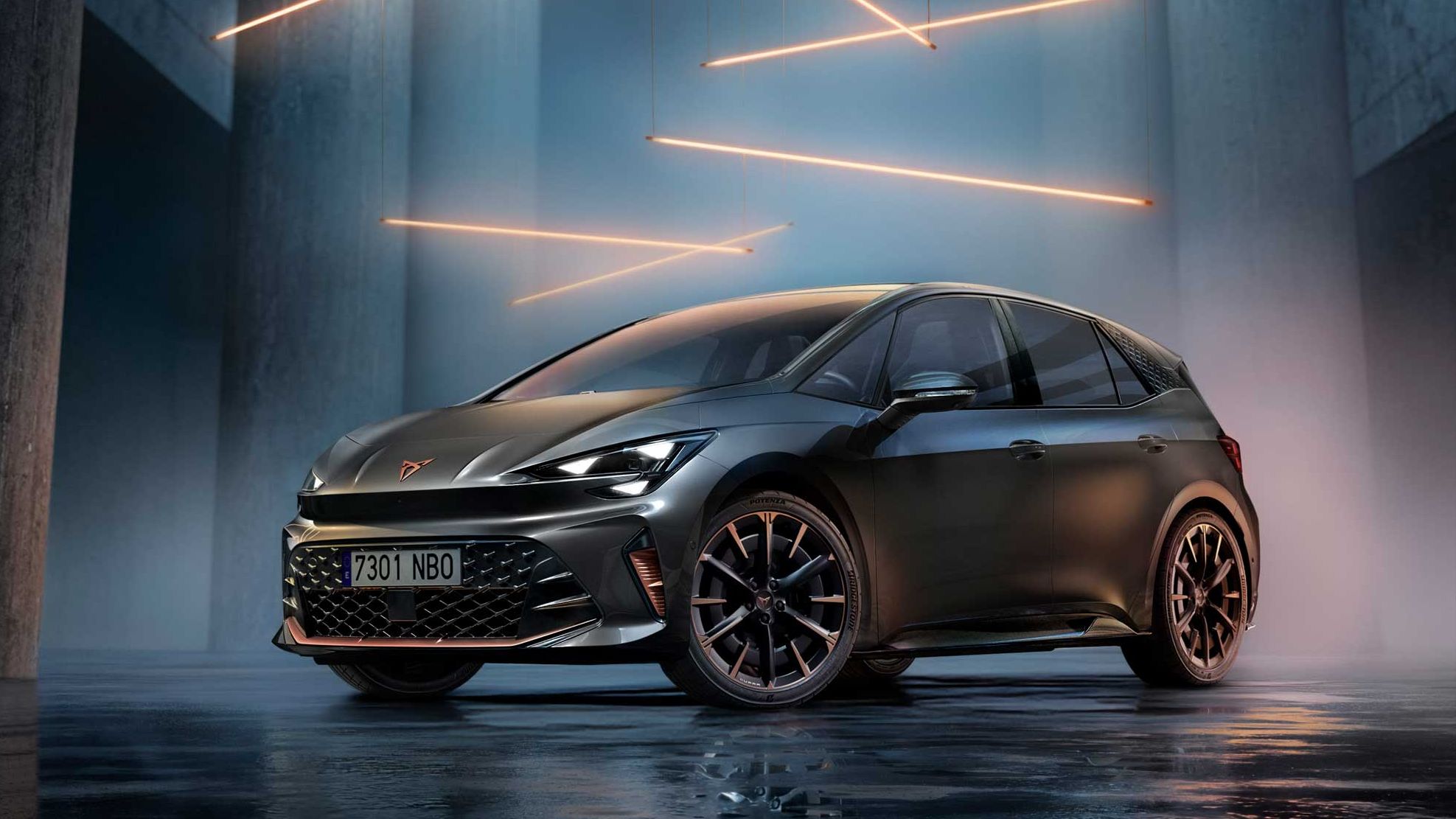 Temno siv CUPRA Born stoji v futurističnem, zatemnjenem prostoru z visokimi betonskimi stebri. Nad njim visijo tanki oranžni svetlobni trakovi, ki osvetljujejo bleščečo karoserijo in kovinska platišča. 