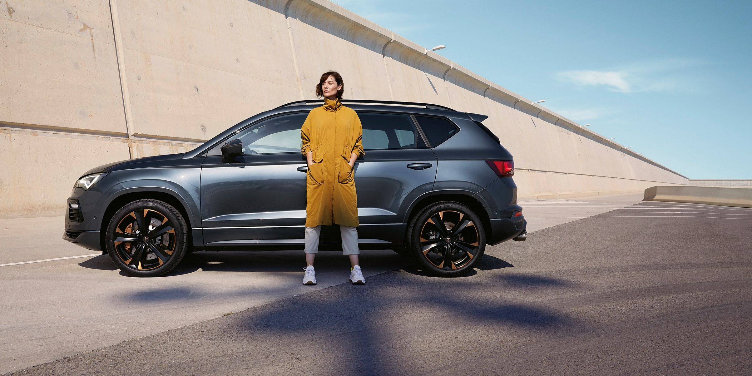 Ein CUPRA Ateca in grau, eine Frau steht davor.