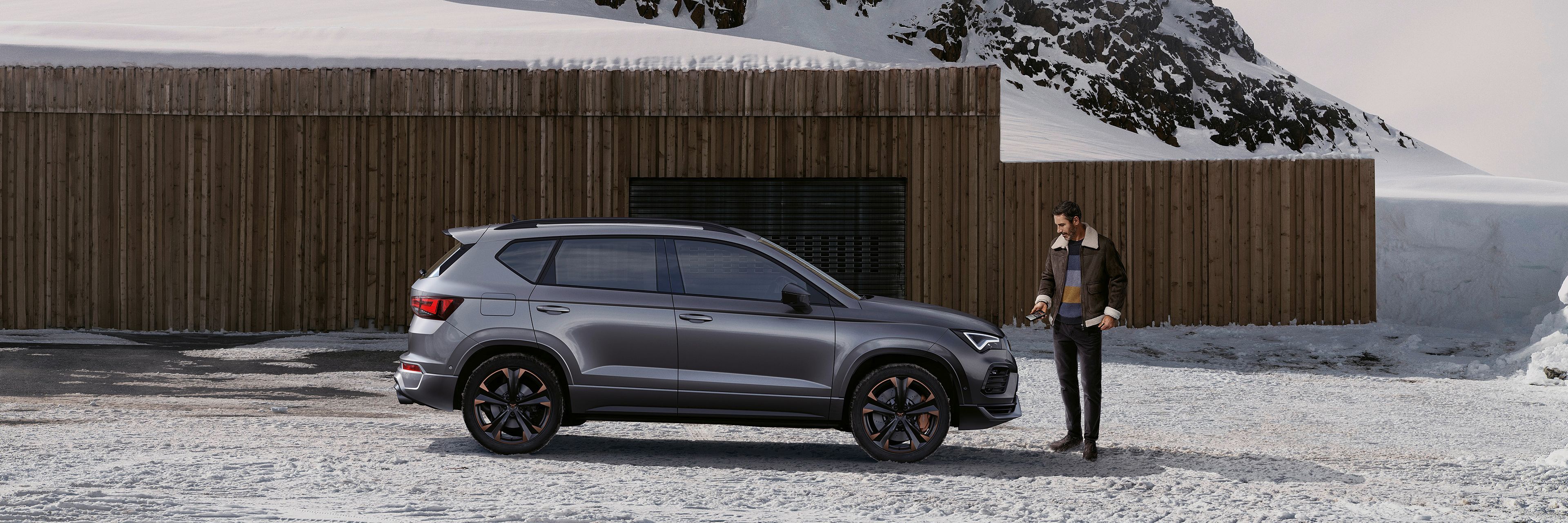 Ein CUPRA Ateca parkt in einer winterlichen Berglandschaft. ein Mann steht vor dem Fahrzeug.