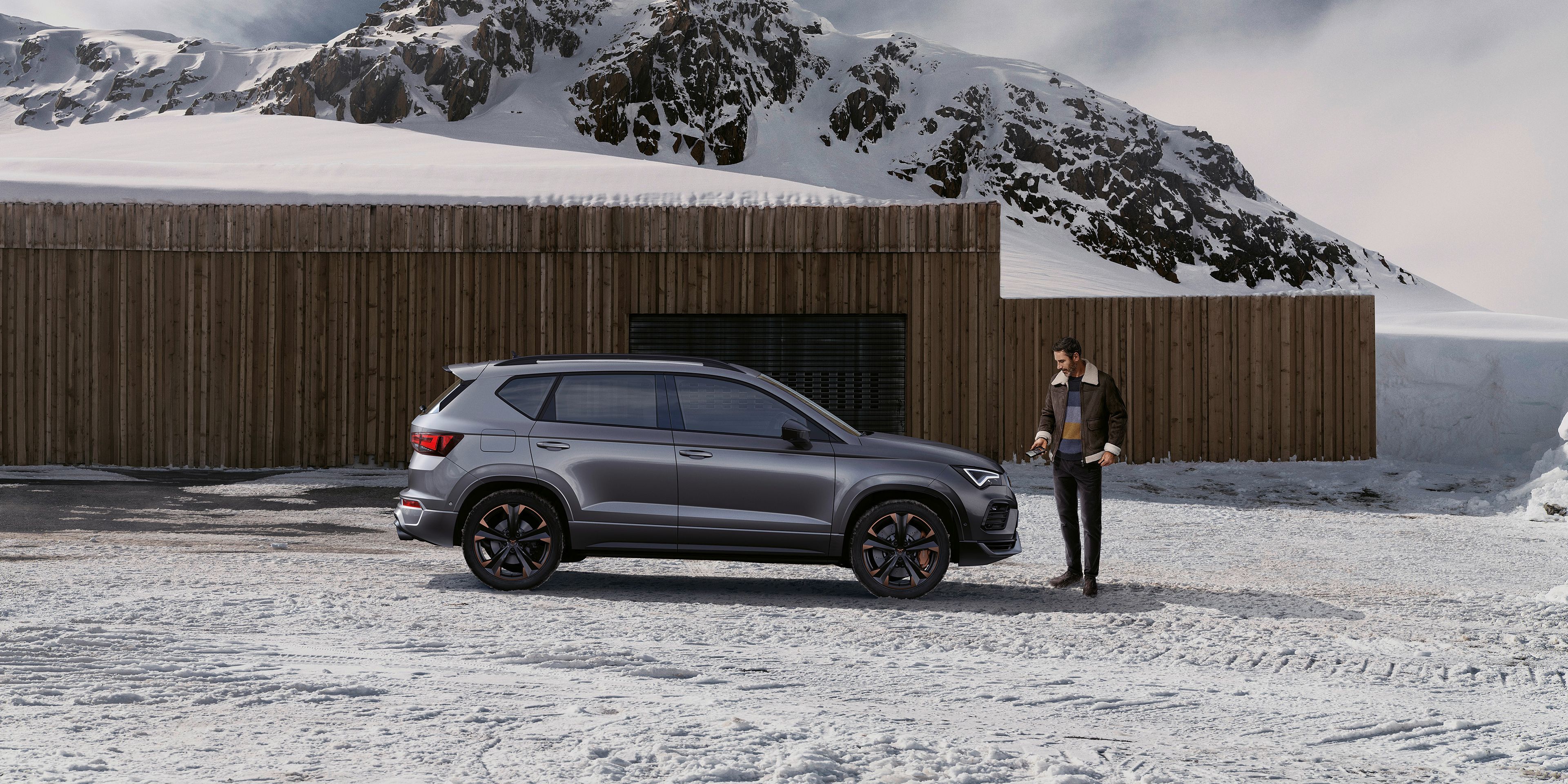 Ein CUPRA Ateca parkt in einer winterlichen Berglandschaft. ein Mann steht vor dem Fahrzeug.