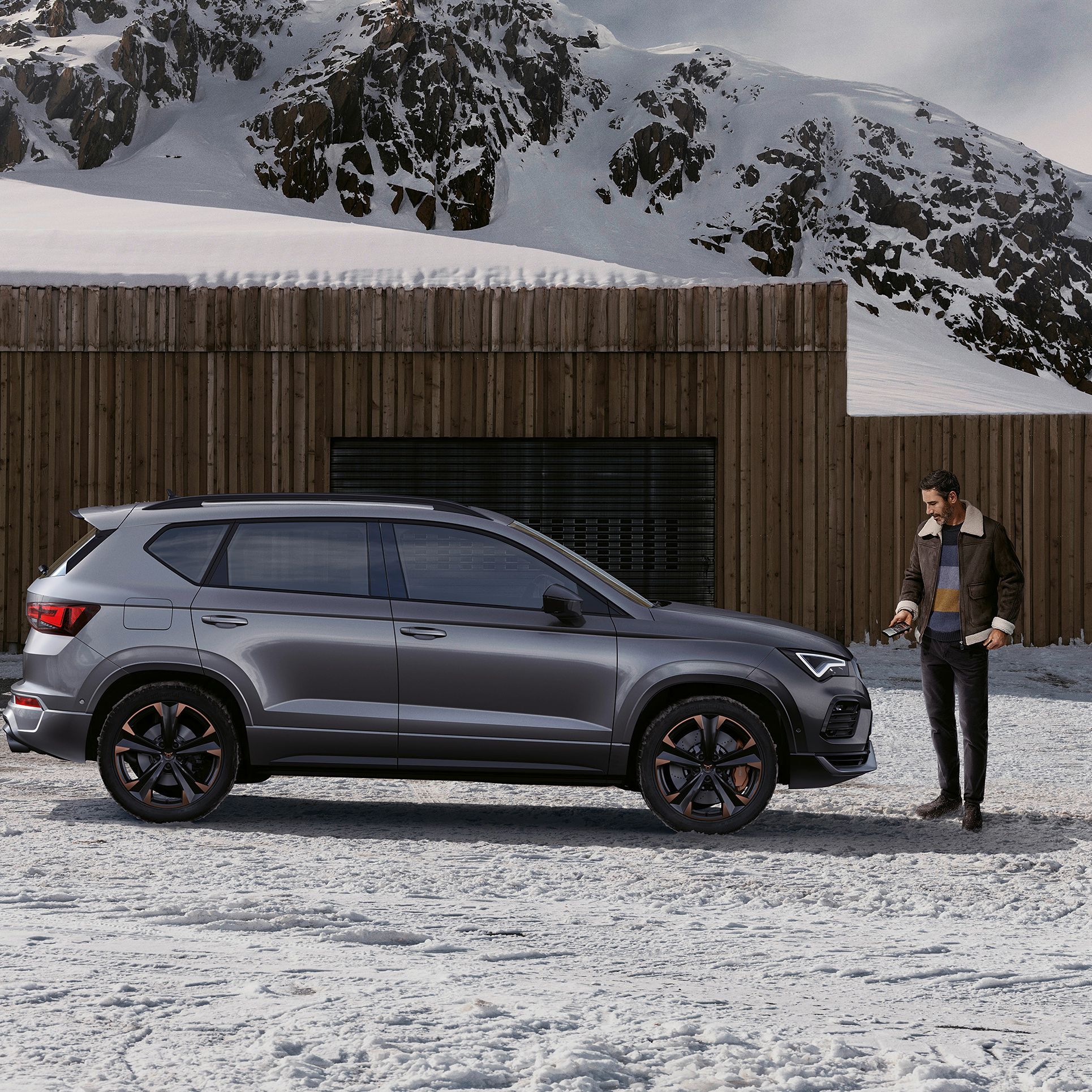 Ein CUPRA Ateca parkt in einer winterlichen Berglandschaft. ein Mann steht vor dem Fahrzeug.